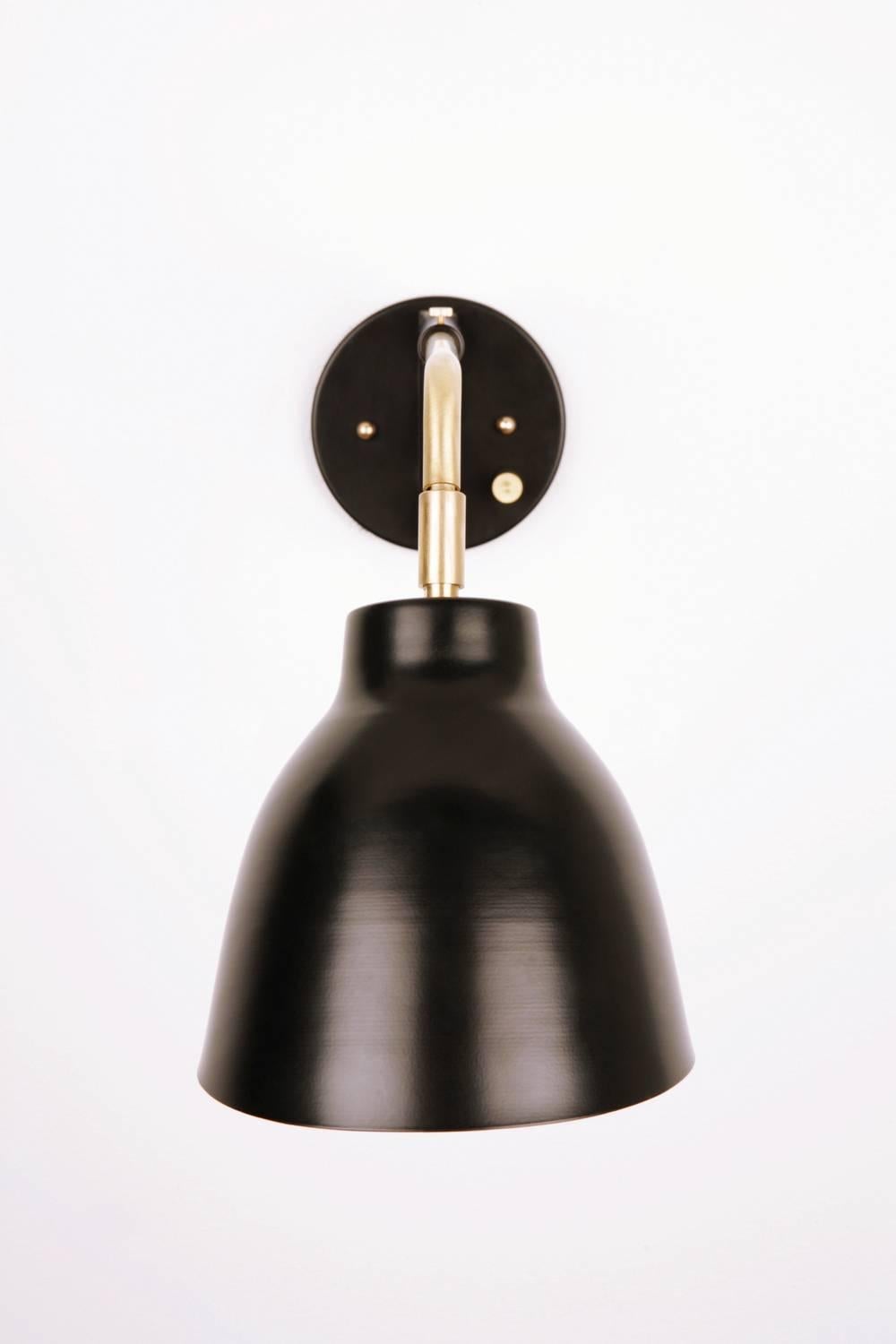 The navire jib sconce is part of Atelier de Troupe's Classic Navire collection inspired by nautical lamps from the 1930s. The fixture has a solid brass arm and up and down tilting shade. Shade options are uncoated brass or powder coated black. The