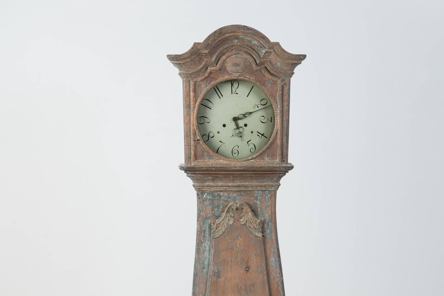Early Swedish rococo long case clock manufactured during the early rococo period when there still were influences from the baroque period. Case in straight shape with carved wooden rococo decor and the hood with curved top. Scraped to original paint
