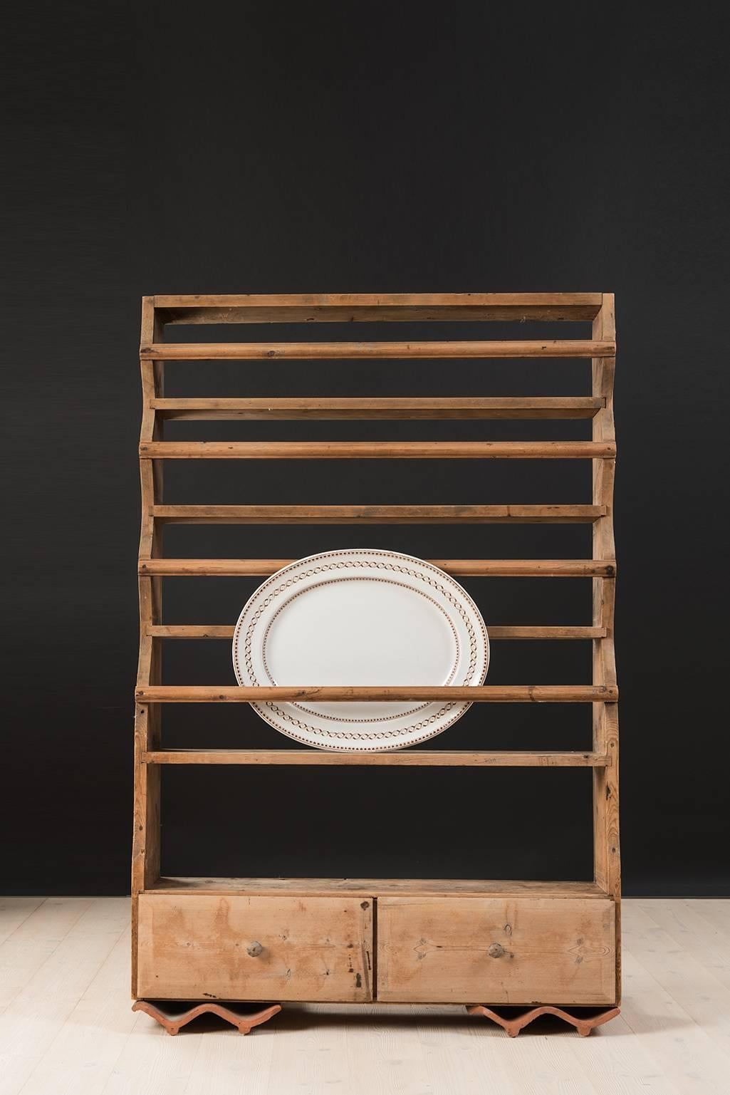 Unusually large plate shelf in pine from the early 1800s. The shelf has never been painted and has its origin in northern Sweden. It is meant to hang on a wall or stand on a bench.