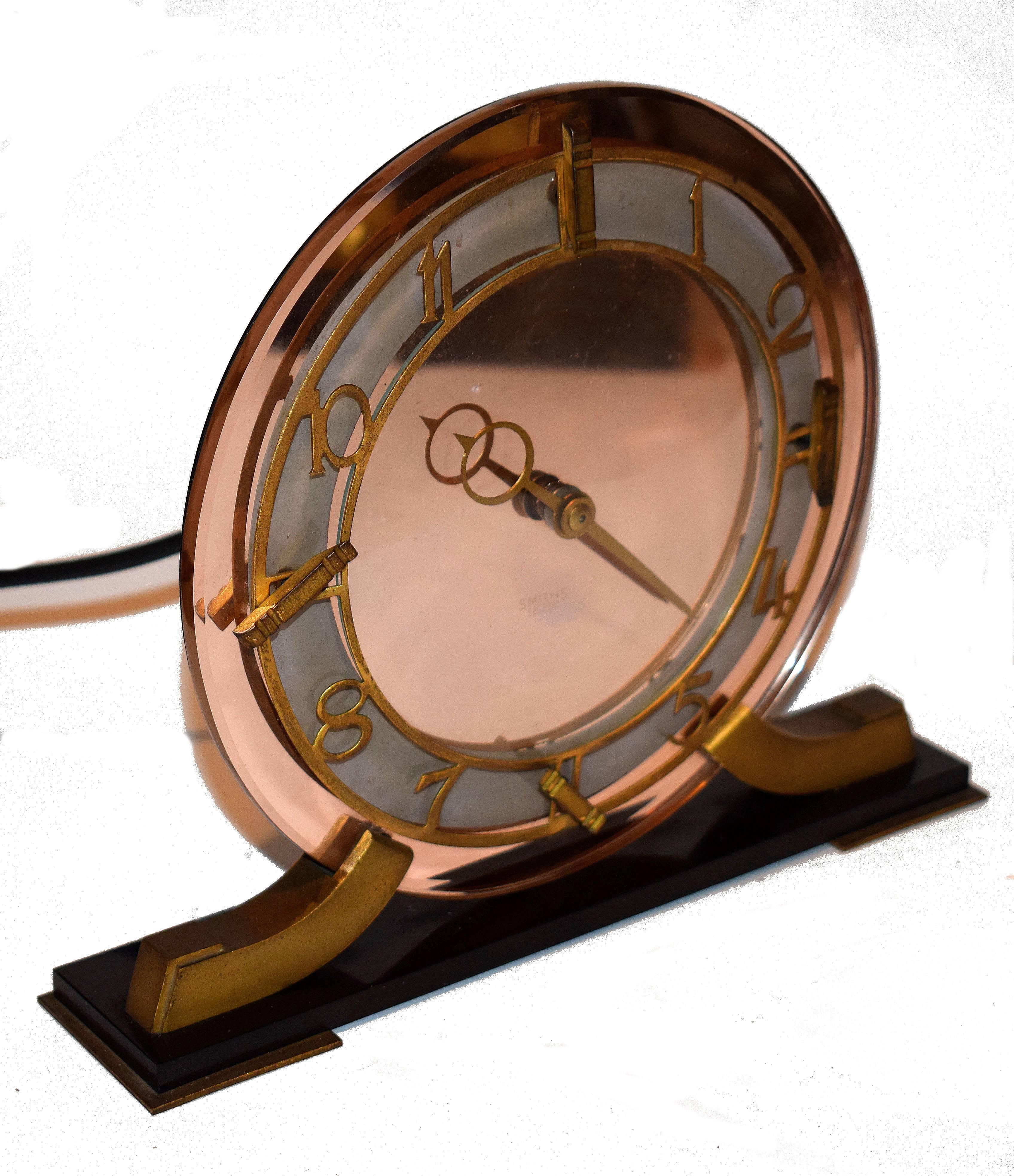 Very attractive and glamourous 1930s Art Deco Modernist clock by Smiths, an English maker. Runs on electric so no winding needed. Features a heavy thick pink mirror glass face with gilded Bezel and black plinth. The condition is excellent, showing