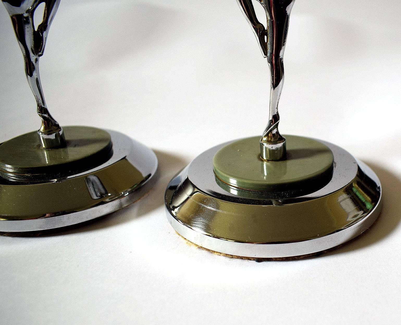 Fabulous pair of English Art Deco figural candlesticks feature bookended female nudes modelled in relief. They pose on one leg and hold aloft a black Bakelite bead and green marbled Bakelite disc. This in turn supports a chrome bobeche and candle