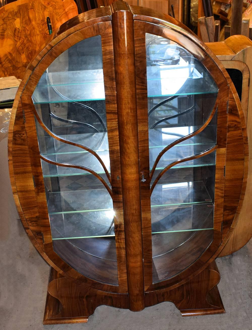 Very rare example of what is considered one of the more rare Art Deco display cabinets is this oval shaped heavily figured walnut veneered example. This particular one is even more scarce having still retained it's original mirror back, giving that