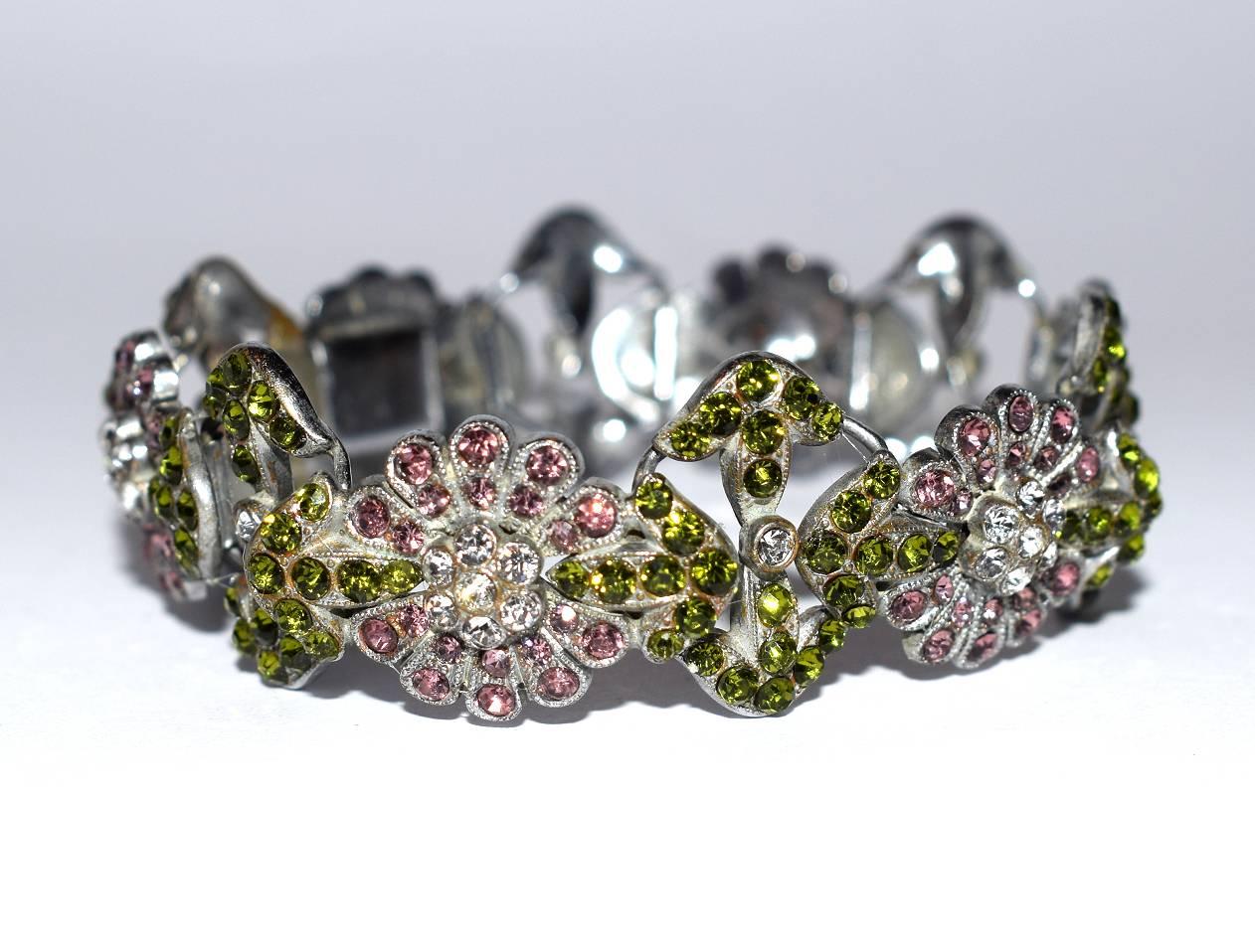 For your consideration is this beautiful 1930s Art Deco multicolored stone ladies bracelet. A hinge clip fastens the bracelet at the back. Alternate flower heads in ruby red and green with clear stones making the accent to the bracelet. Condition is