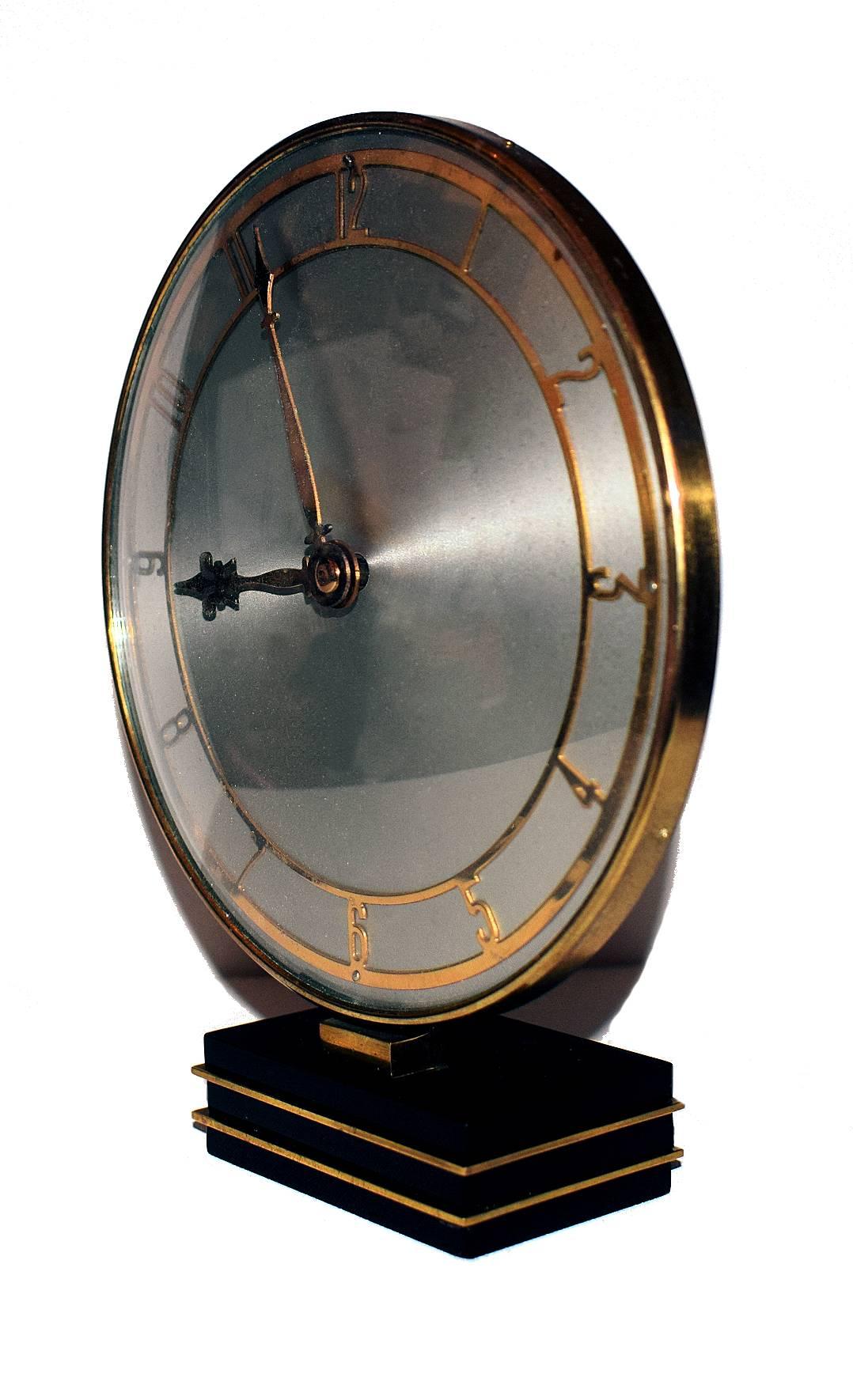 Very attractive modernist English wind up movement clock. Brass chapter ring and a silvered dial makes the back drop to the gold tone metal chapter ring and numerals. The whole clock sits on a black and gold tone celluloid base. Keeps good time