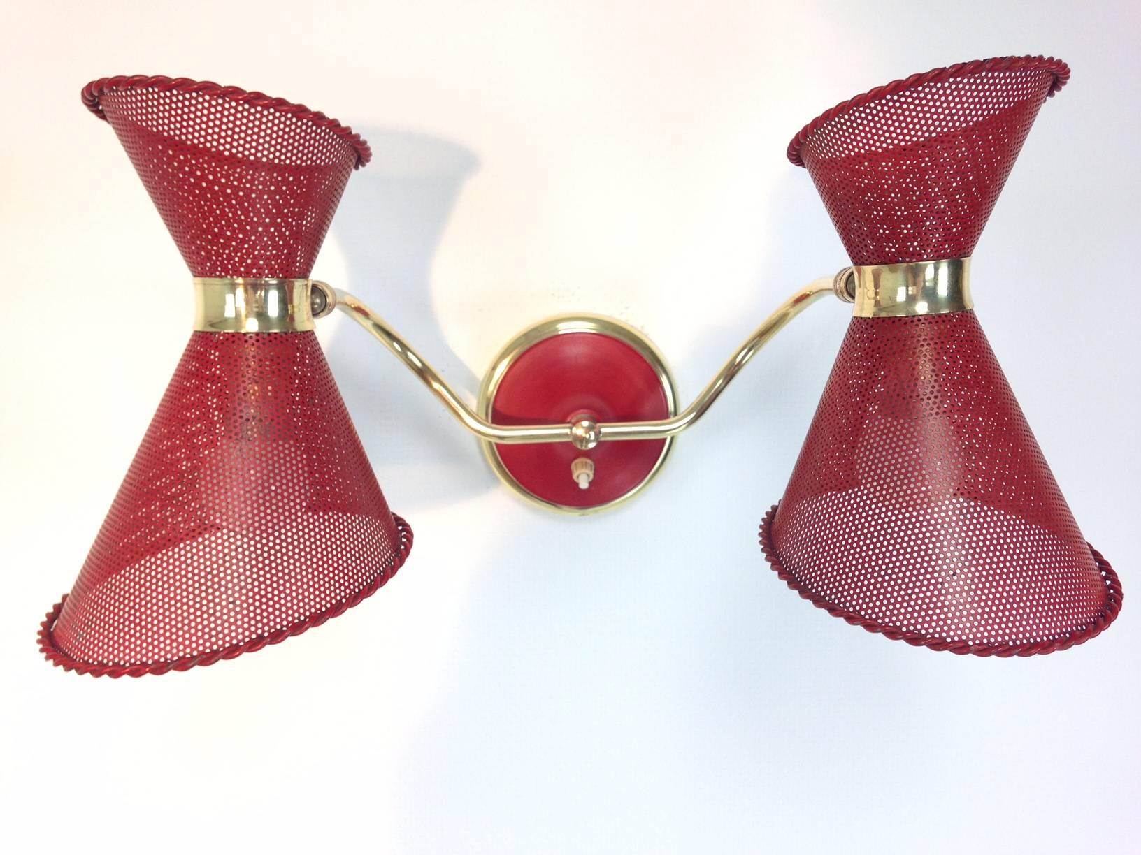 French wall light in the style of Mathieu Mategot. The piece features rotatable, red varnished and perforated diabolo shades of metal, and is supported by brass arms and a plate. The width is variable from 42 cm to 52 cm.

We ship worldwide, do not