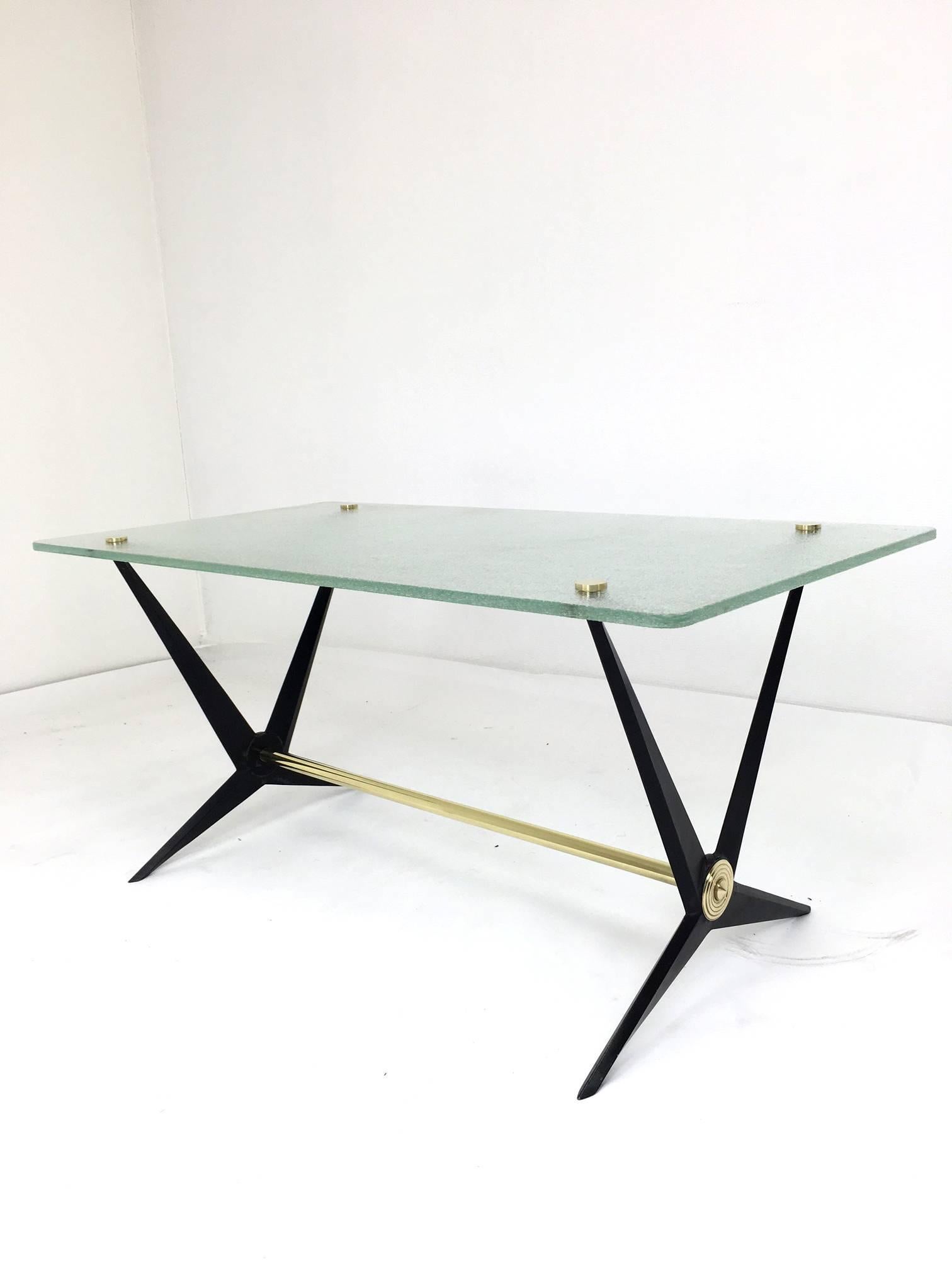 This back cast iron and brass side table was designed by Angelo Ostuni. It has a tempered glass top with slightly rounded corners and four brass circular fittings to secure the glass to the base. There is brass decorative detailing on the
