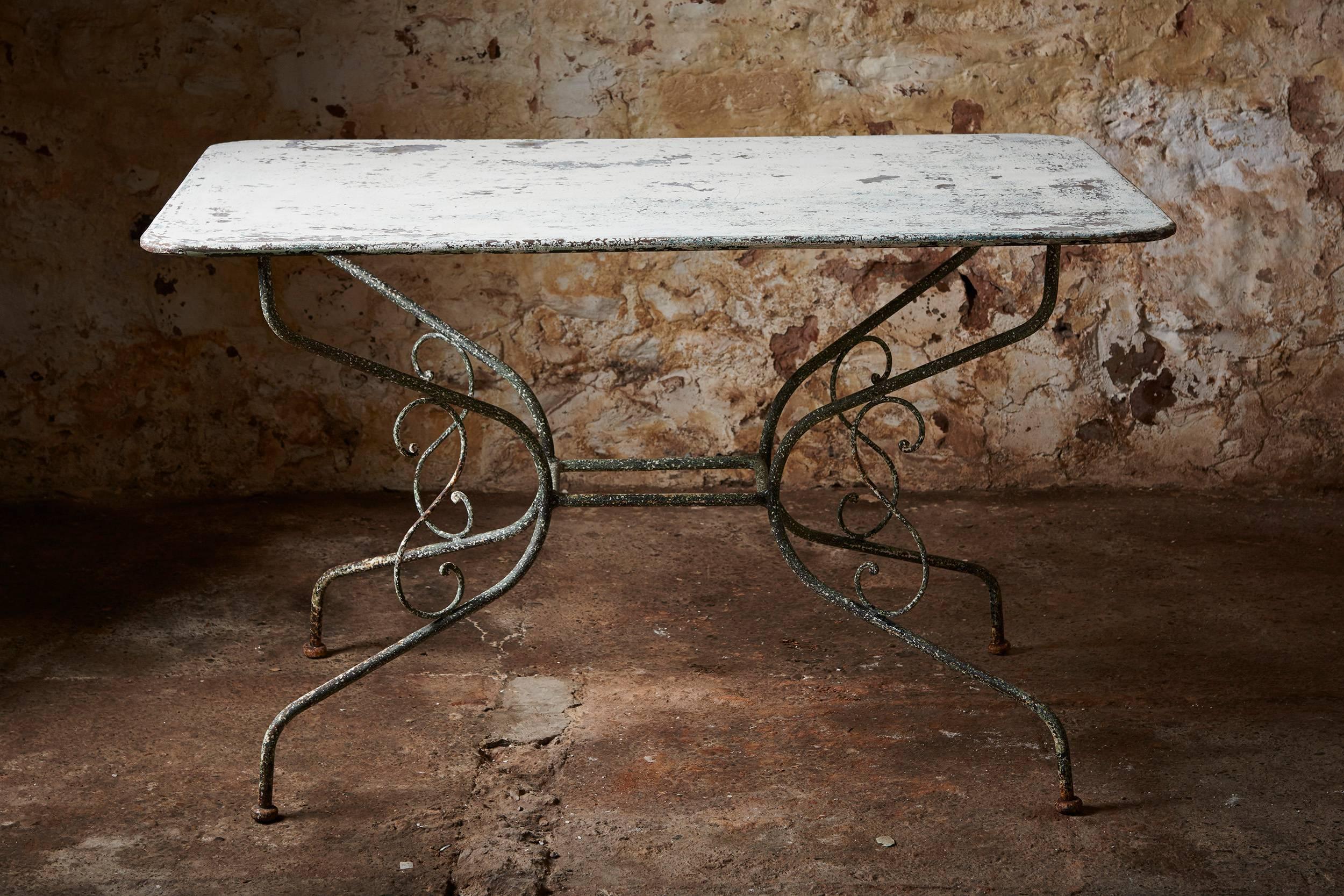 A stunning 19th century dining table, with its original painted patina. The loose and flaking paint was removed to reveal the earlier painted metal top. The frame is hand-forged, with elegant scrolls.

We found the appealing little dining table in