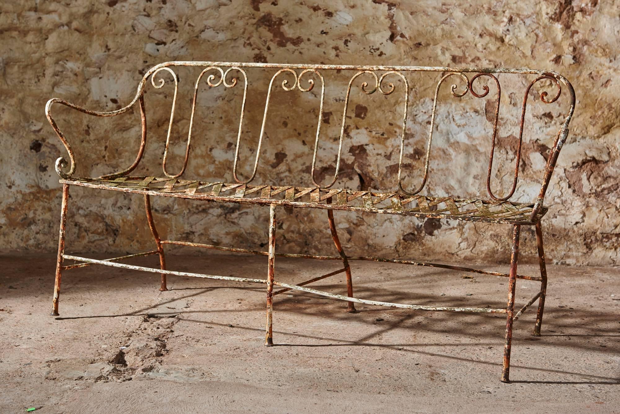 A very attractive wrought iron French garden bench in very good condition featuring an authentic original patina. This bench was manufactured in and around 1860 and has an attractive hand-forged scrolled back with a latticework seat. Its simple