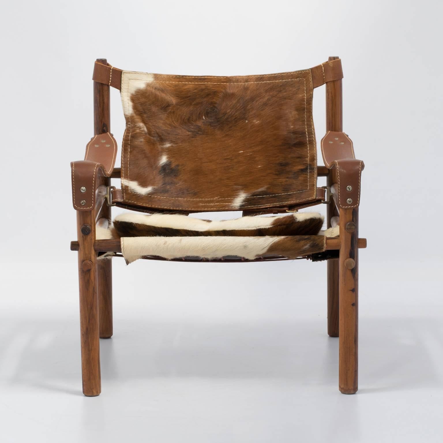 Fabulous Sirocco safari chair by the Swedish designer Arne Norell in rosewood and a lush hair-on-cowhide. This chair has a beautiful rustic modern vibe; the brindle cowhide is so perfect with the rosewood, bronze hardware and white over-stiching on
