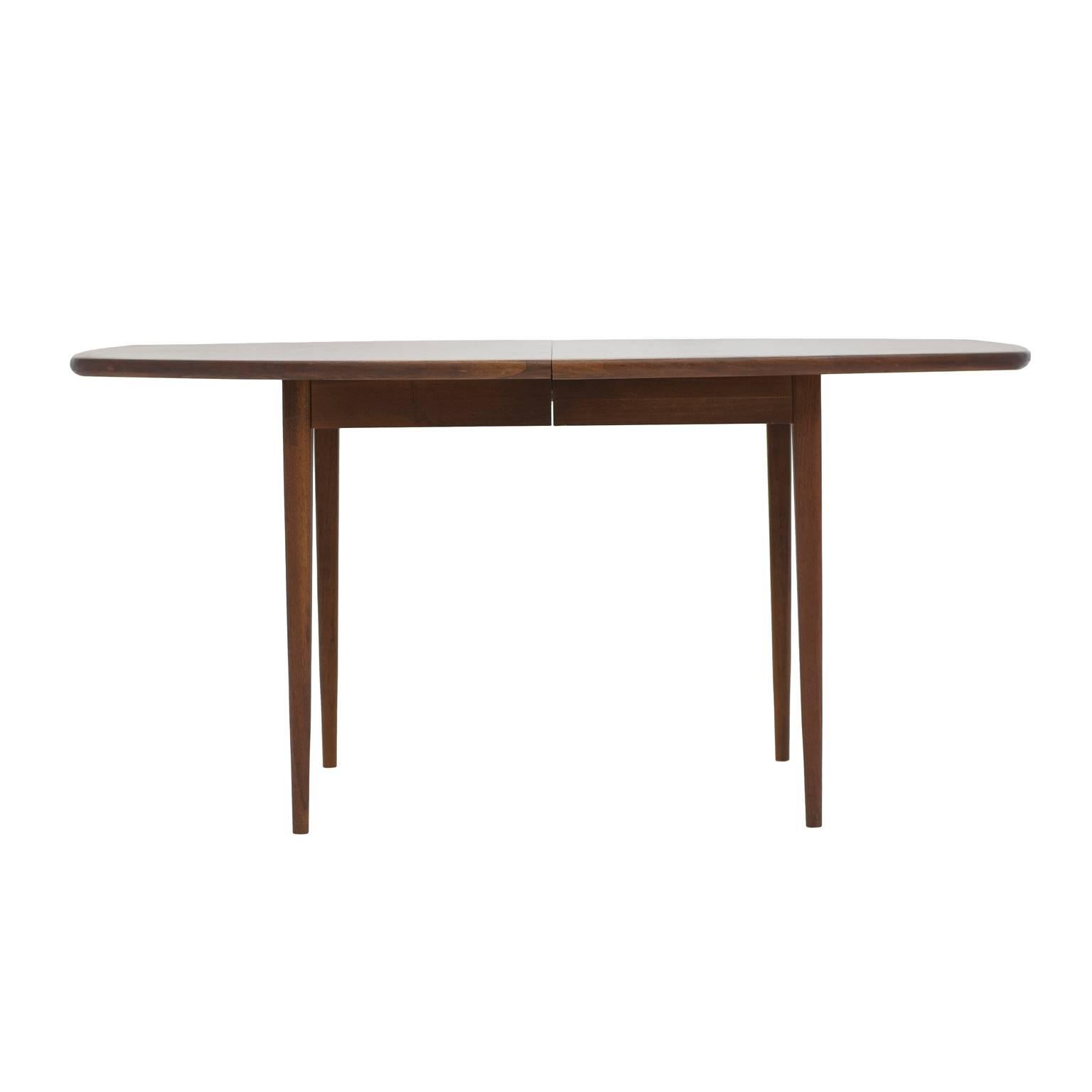 Modernist, elegant and streamlined Mid-Century dining table by Dillingham in solid walnut. The table design is attributed to Milo Baughman and features tapered legs and a surfboard style top. This dining table has two leaves, each 18” wide. With one