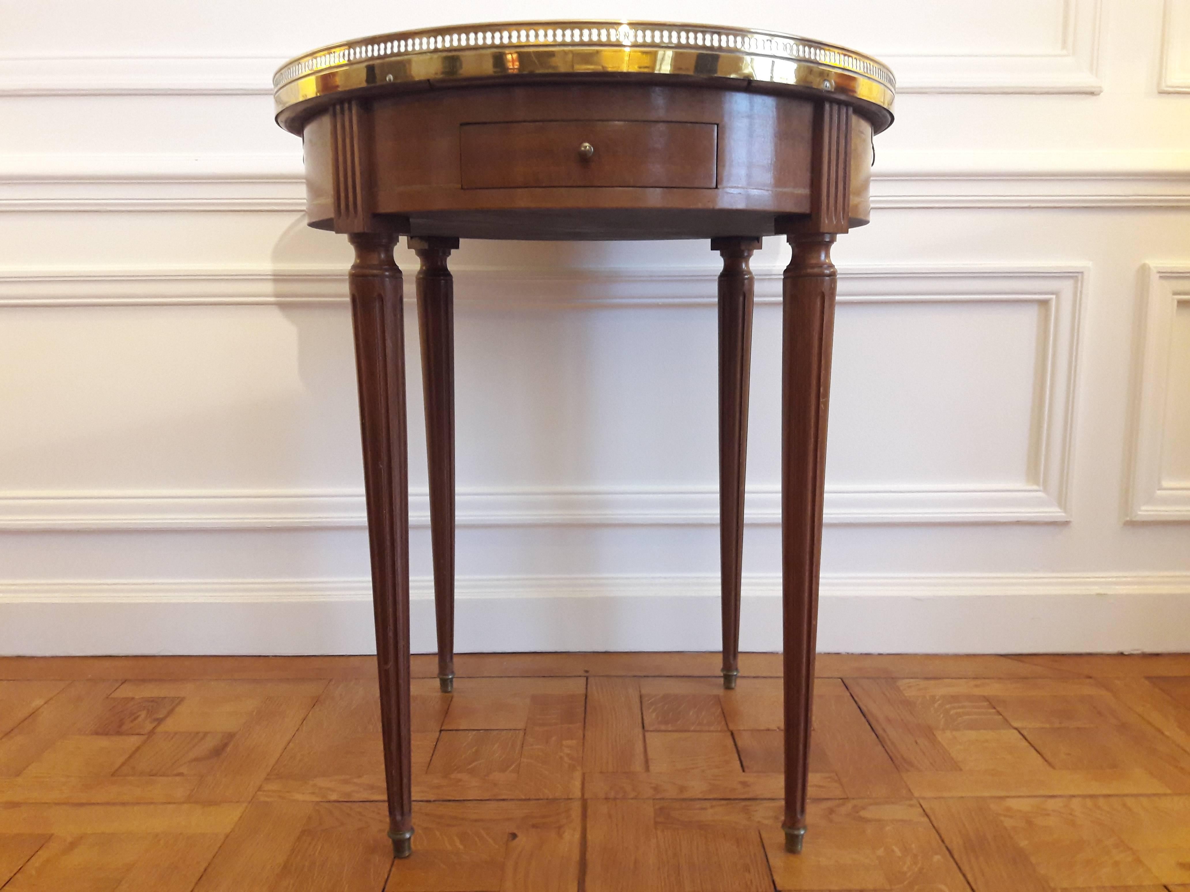 French Louis XVI style bouillotte table with Carrara marble-top. Brass gallery and fluted legs finished with golden bronze clogs. The table has two dove-tailed drawers and two pull-out tablet shaped leaves. The name “bouillotte” comes from a French