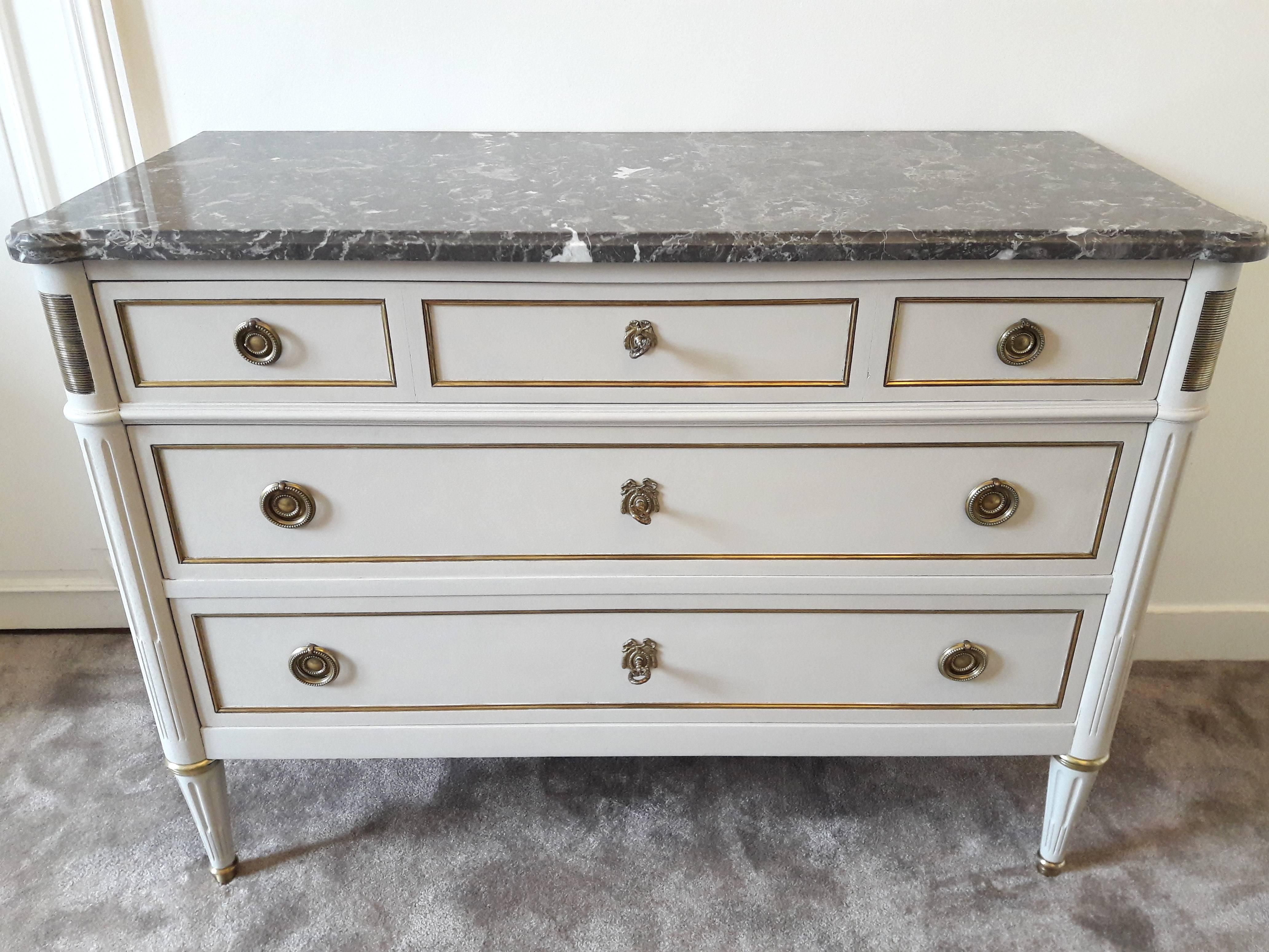 Antique French Louis XVI style chest of drawers topped with a lustrous grey marble, fluted legs finished with golden bronze clogs. Three dovetailed drawers with brass details. 
The first drawer is drawn as if there were three, the woodworking and