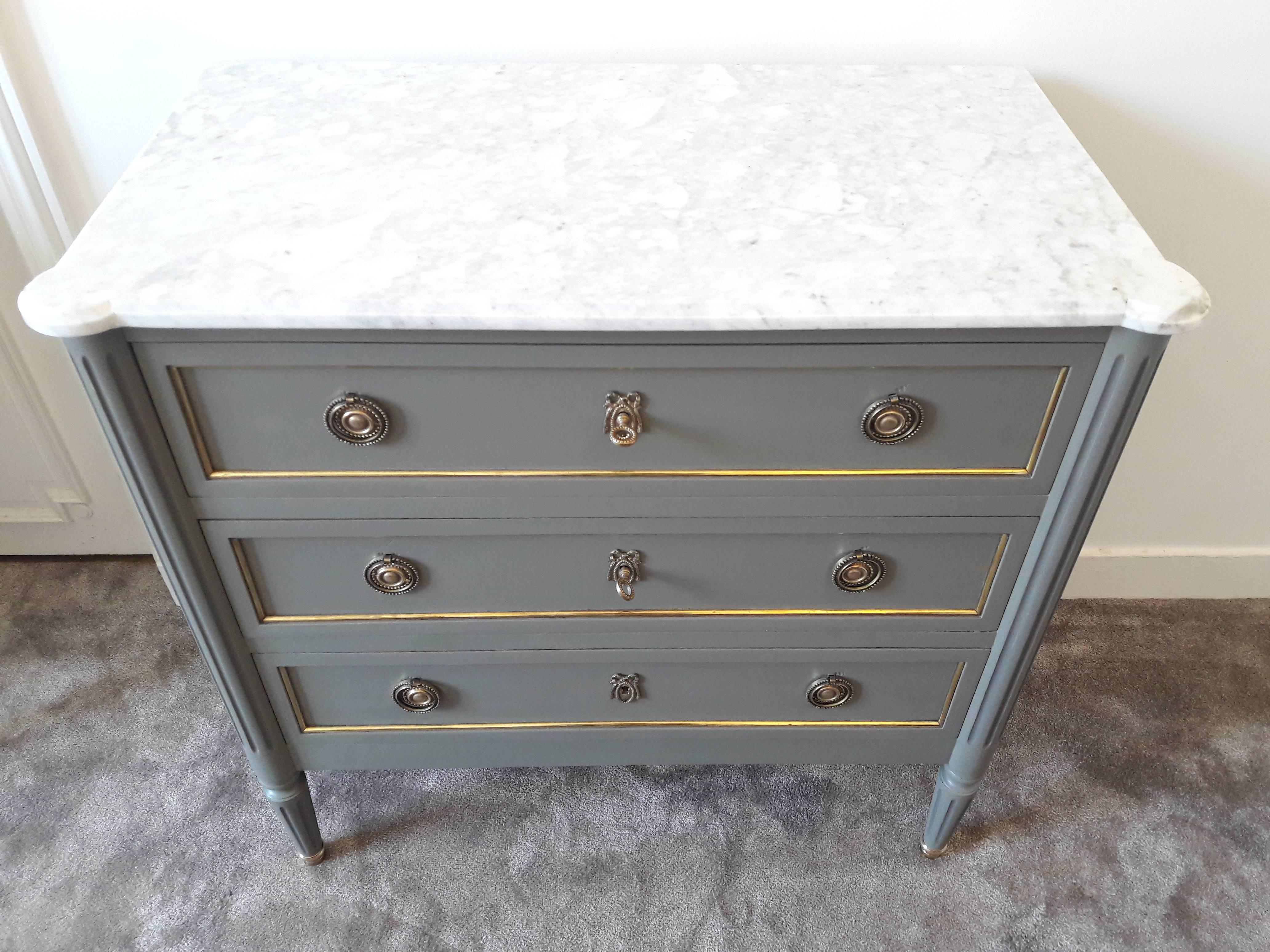 Antique French, Louis XVI style chest of drawers topped with a white Carrara marble, fluted legs finished with golden bronze clogs. 
Three dovetailed drawers with brass details, and three keys.