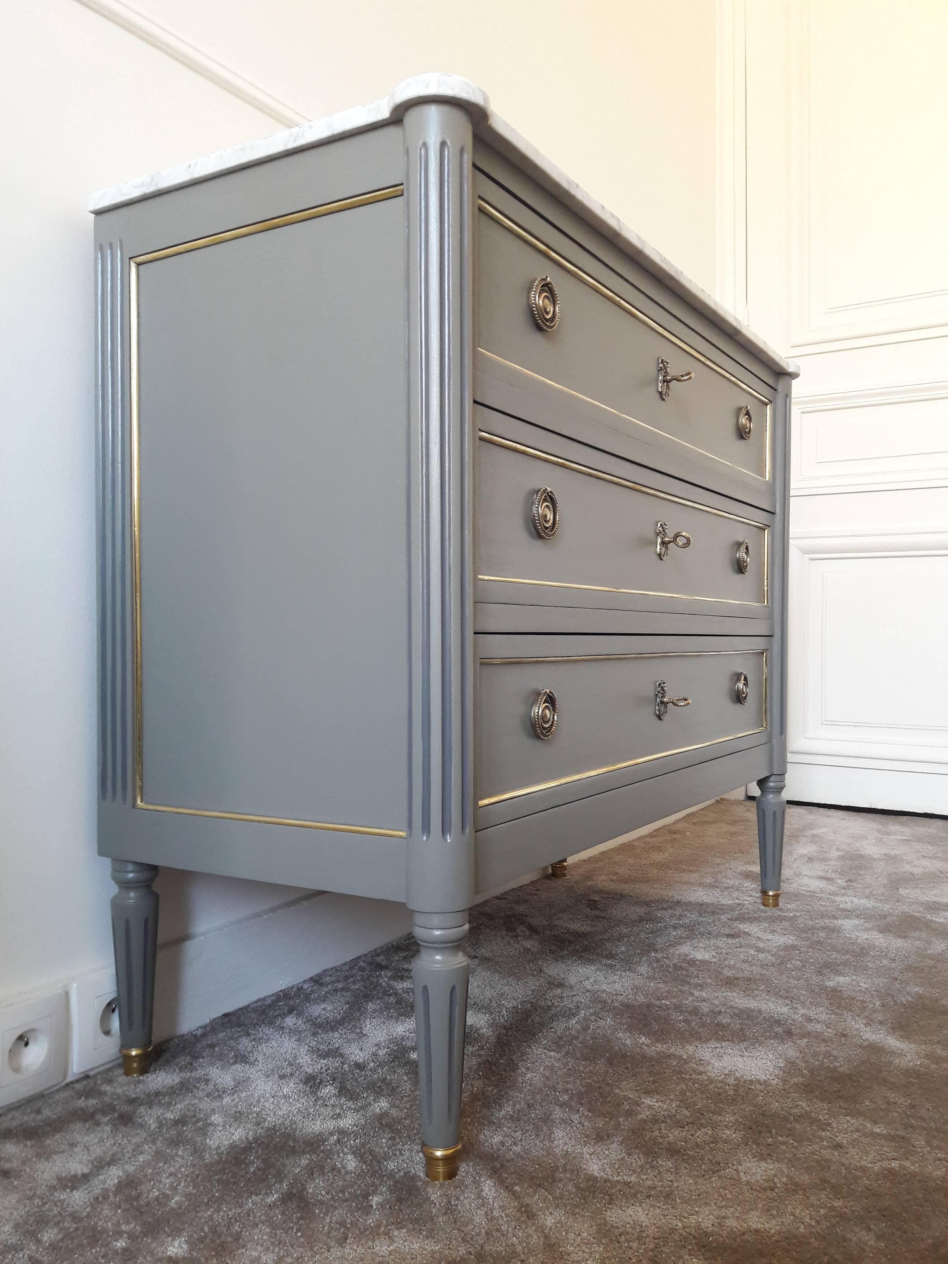 Antique French, Louis XVI style chest of drawers topped with a white Carrara marble, fluted legs finished with golden bronze clogs. 
Three dovetailed drawers with brass details, and three keys.