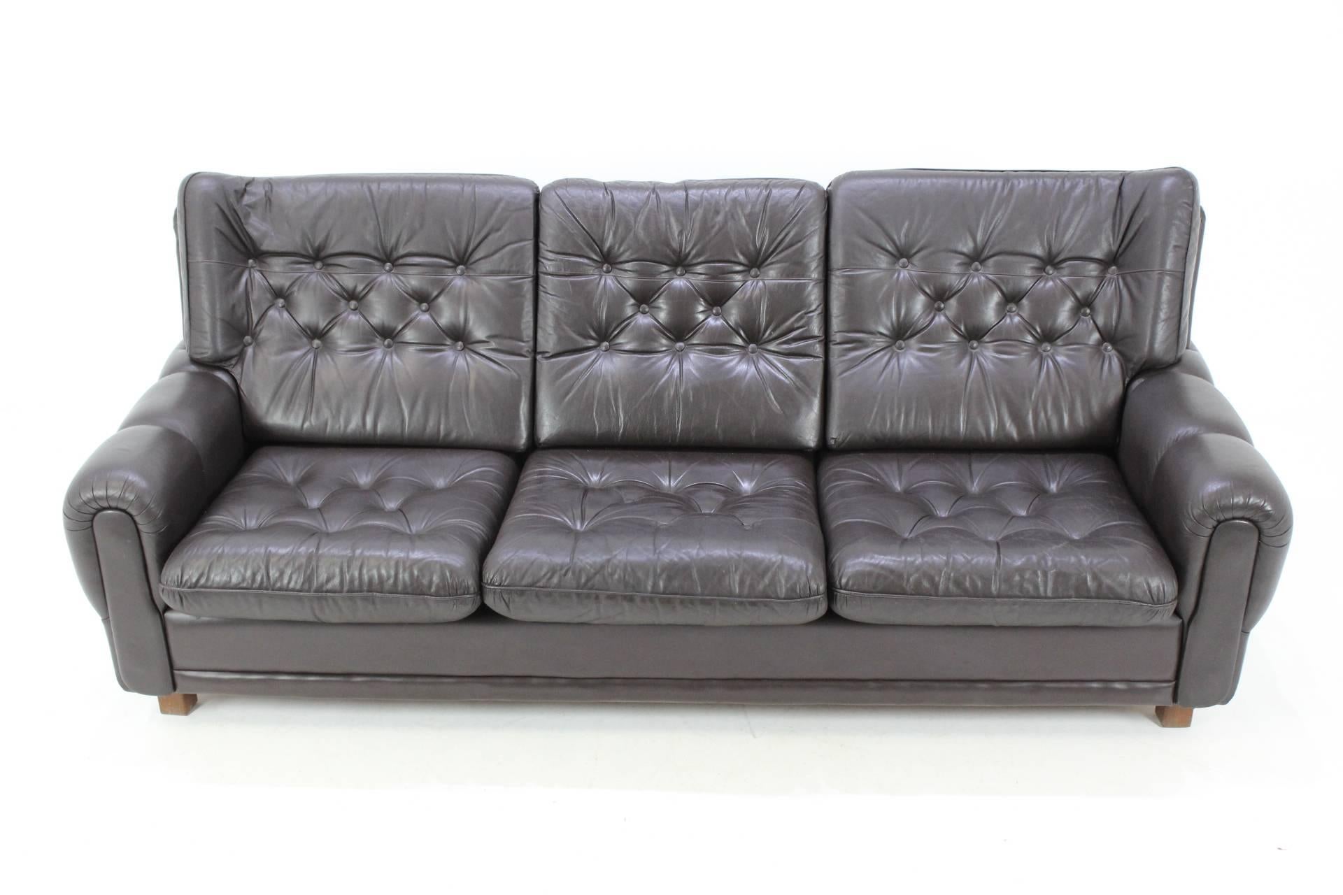 This sofa was produced in Czech Republic during the 1970s. It features a wood structure and brown leather seats.