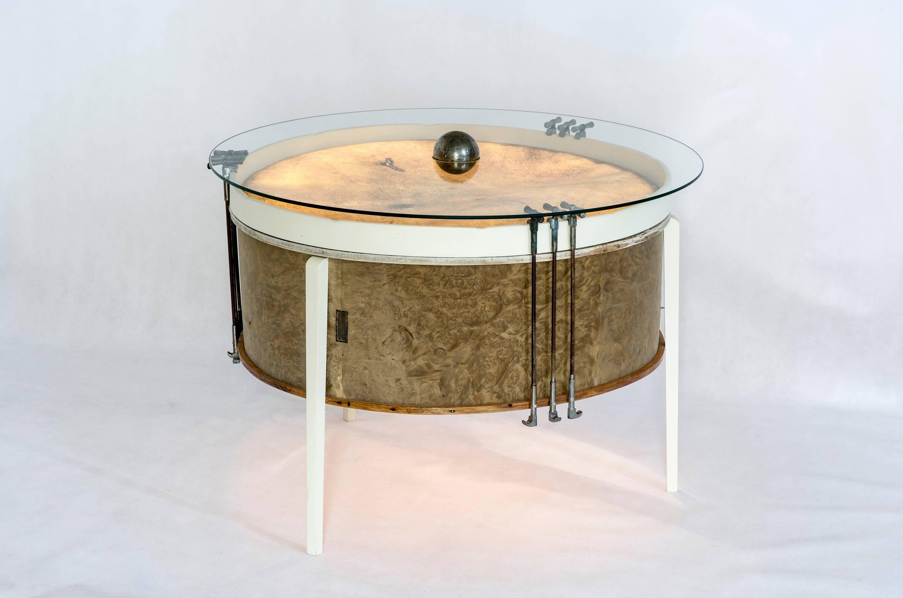 The body of this coffee table is formed by an approximately 100 year old drum. The pedal-drums include original leather membranes, back-lit in order to admire their leather texture as well as the traces of music they once made, the imprint of the