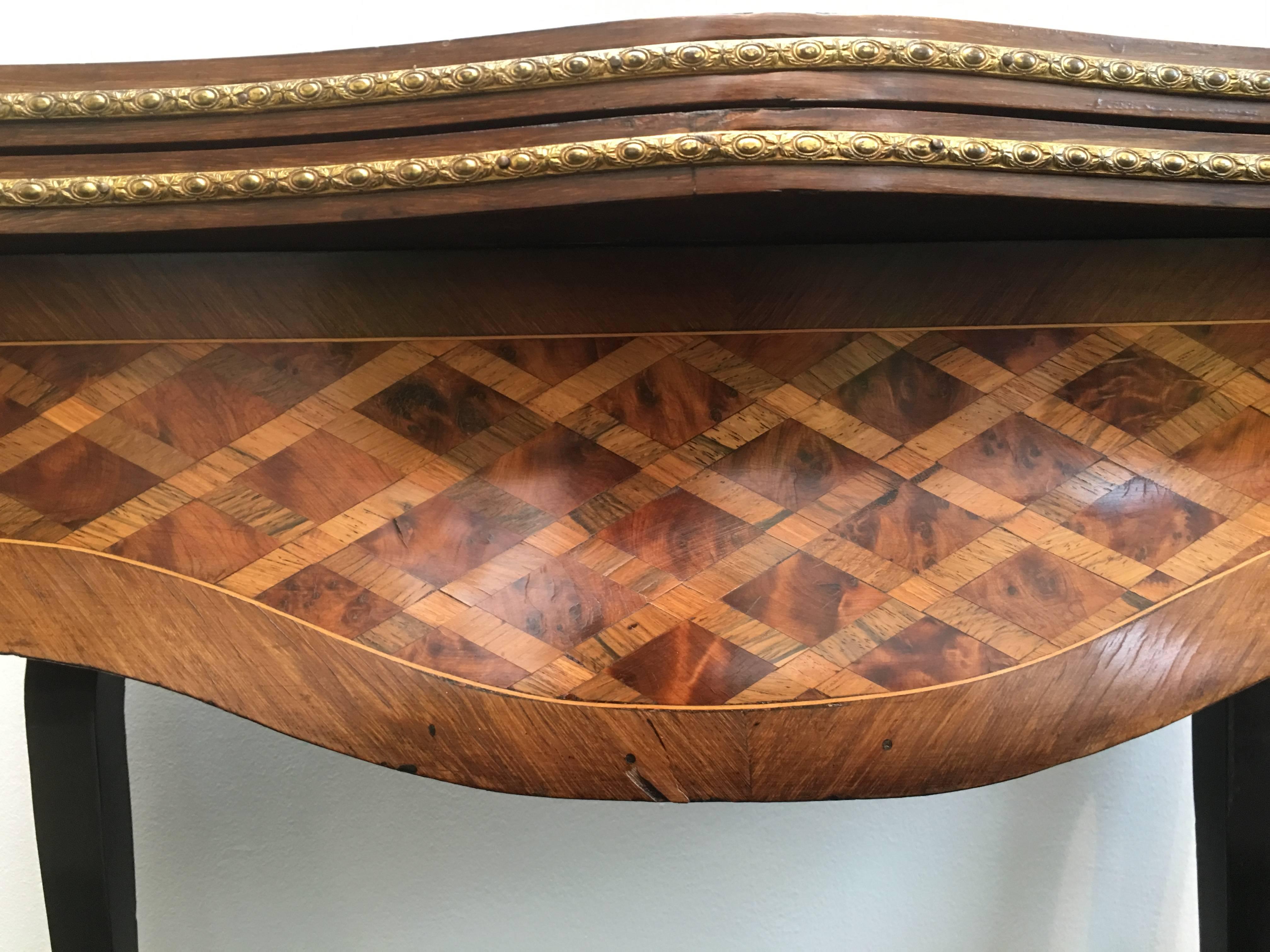 A lovely 19th century parquetry and gilt serpentine fronted fold over French games table in rosewood, satinwood and walnut.

Superb quality, decorated all around, so the table can sit in the middle of a room or behind a sofa and sitting on