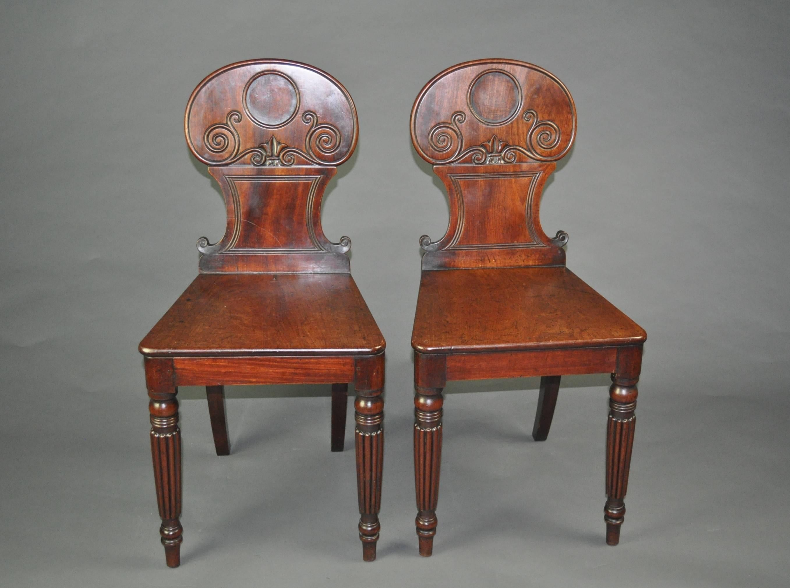 A good pair of mahogany hall chairs, the waisted backs carved with scrolled lines above plain seats with shaped rails. Standing on elegant turned and reeded front legs.
 