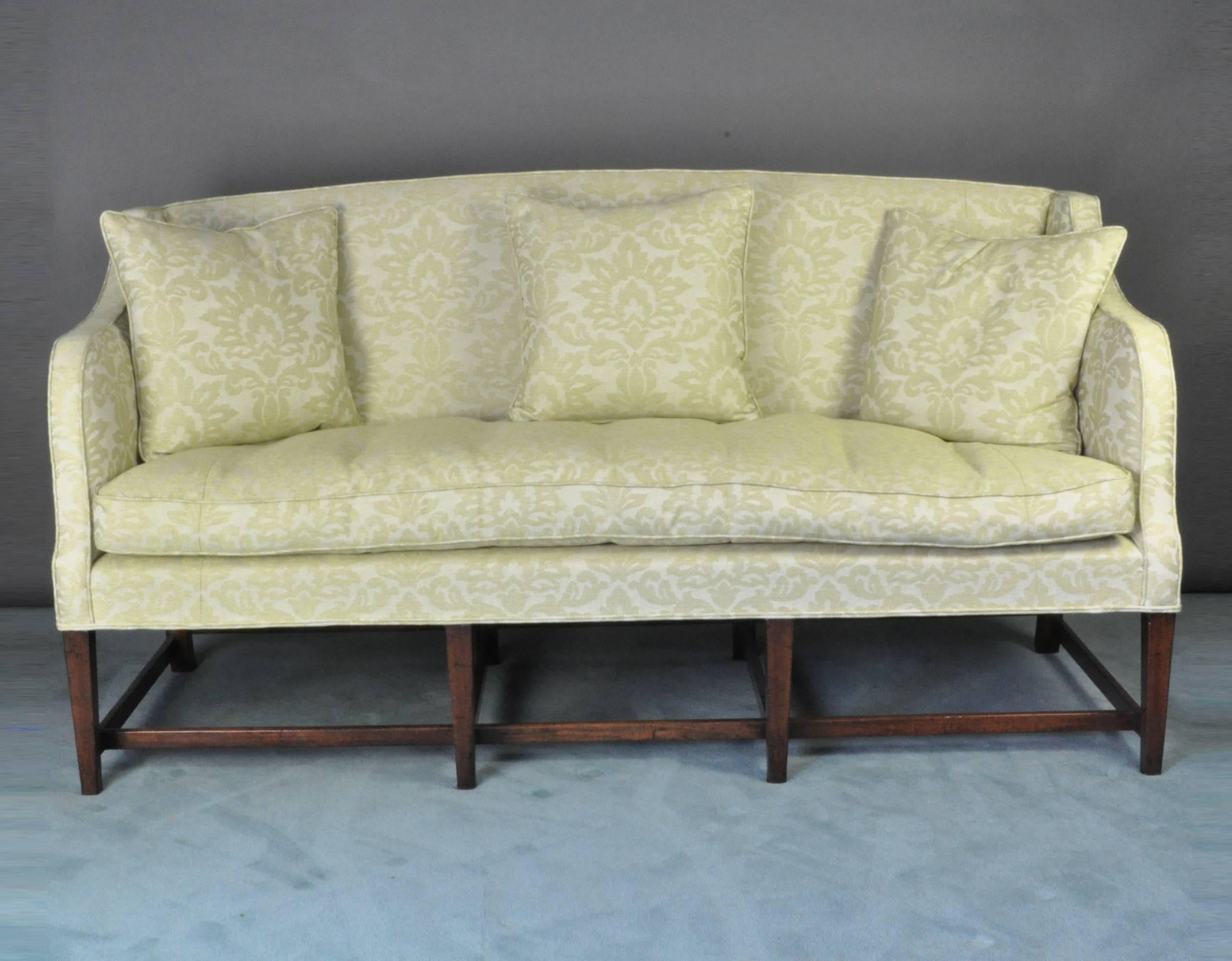A good early 19th century mahogany framed settee or sofa standing on eight square tapering legs, joined by plain stretchers. The shaped back and arms above a bow-fronted seat re-upholstered in soft green damask.
 