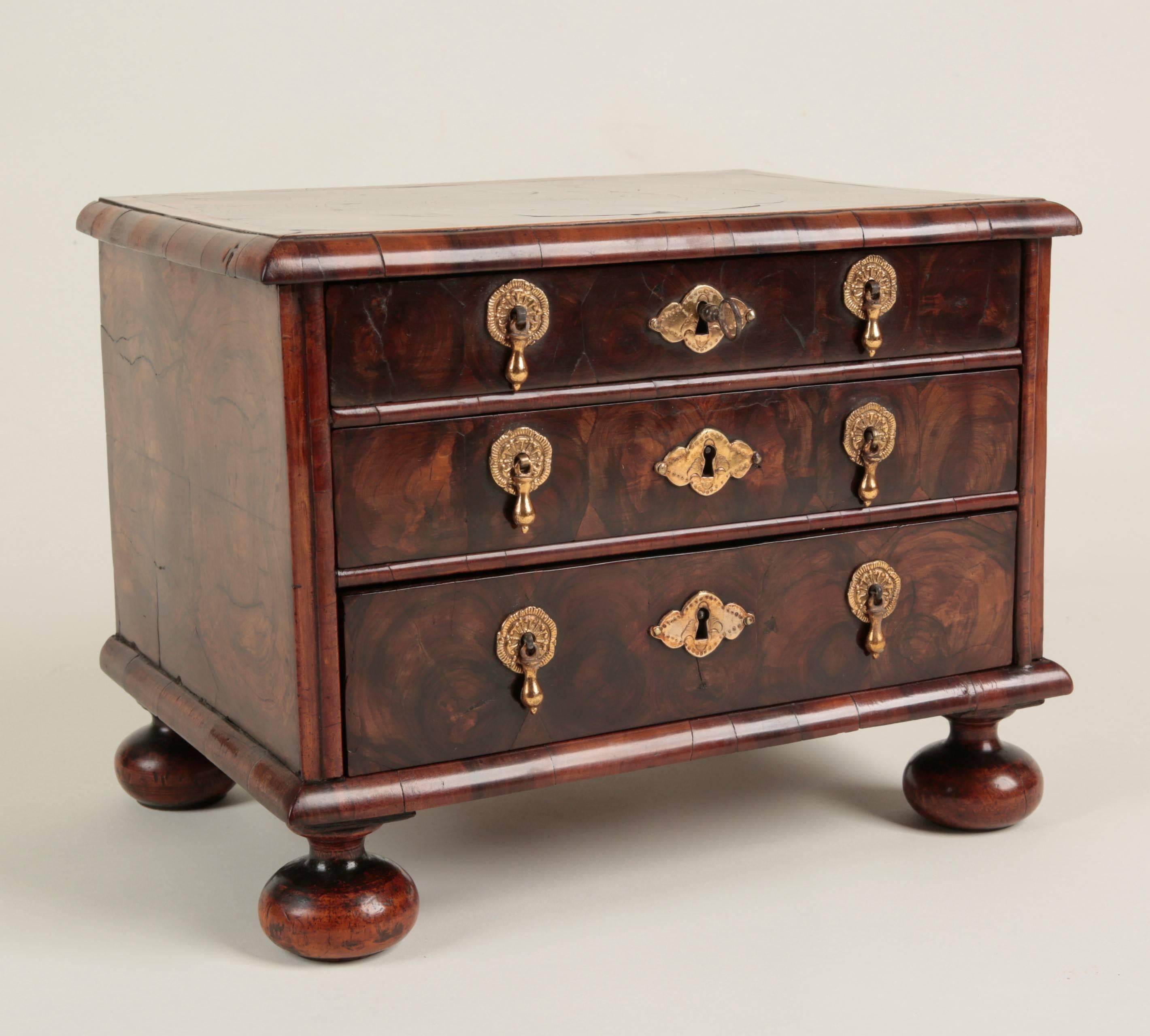 An exceptionally rare William and Mary period miniature chest of applied oyster-cut olive wood. The top and the three graduated oak lined drawers cross-banded with fruitwood. Fitted with original operational locks, the handles and escutcheons