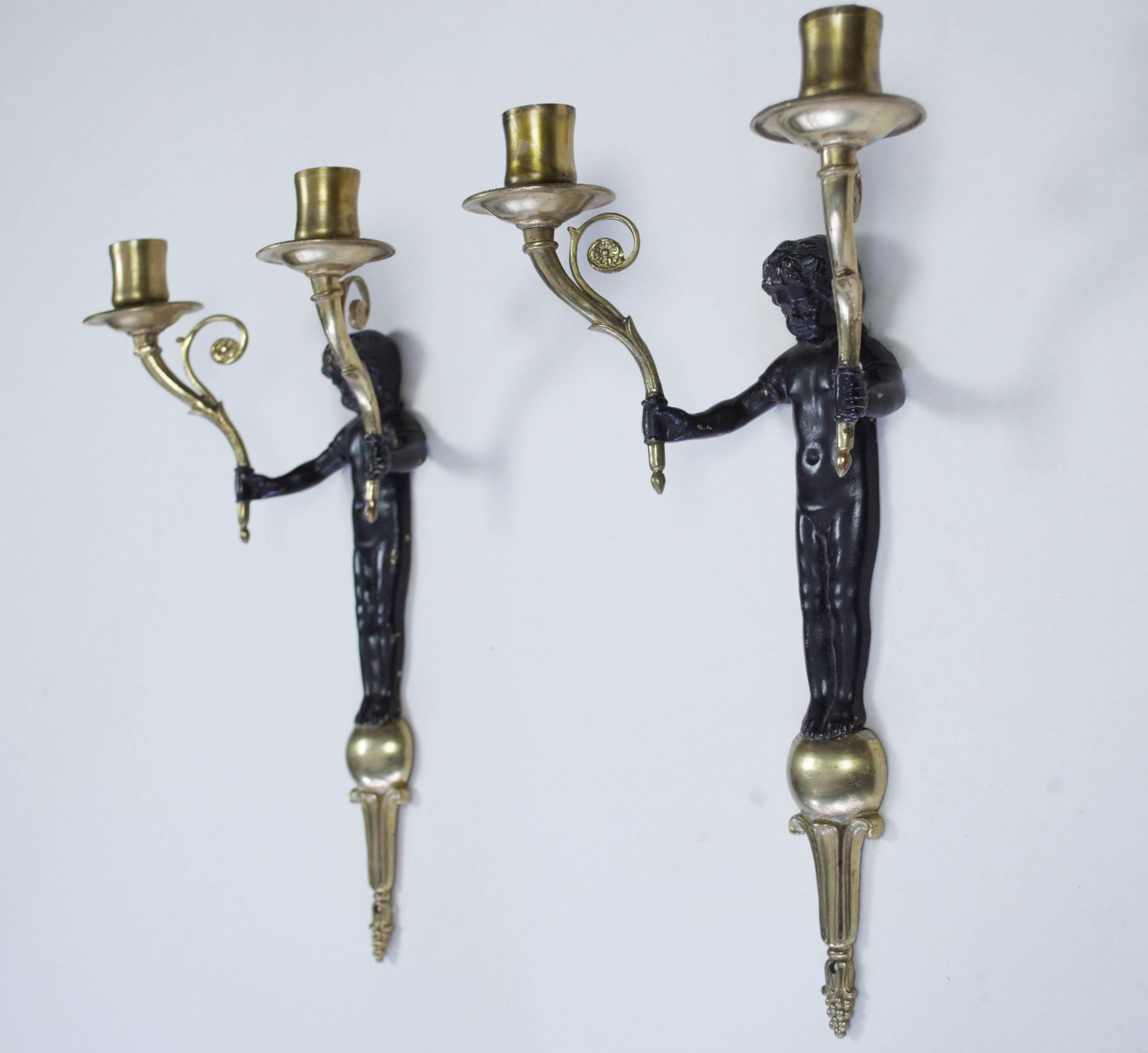 A pair of twin branch bronzed and gilt metal wall lights in the form of putti each holding a candle sconce in each hand.