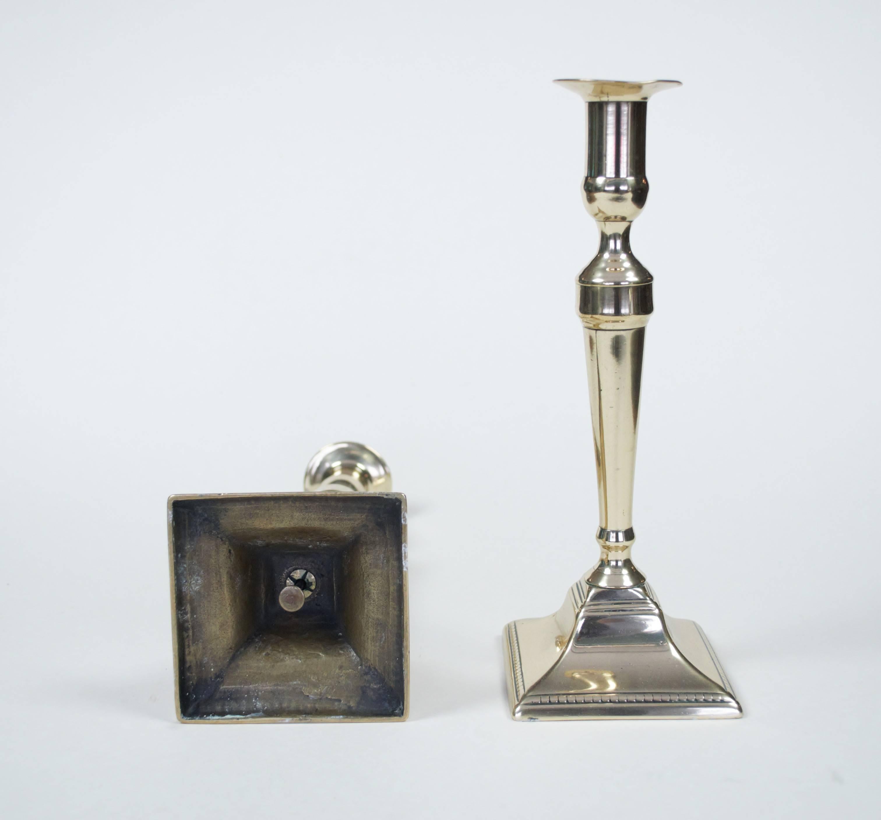 A pair of early 19th century brass candlesticks on square bases with plungers to underside.