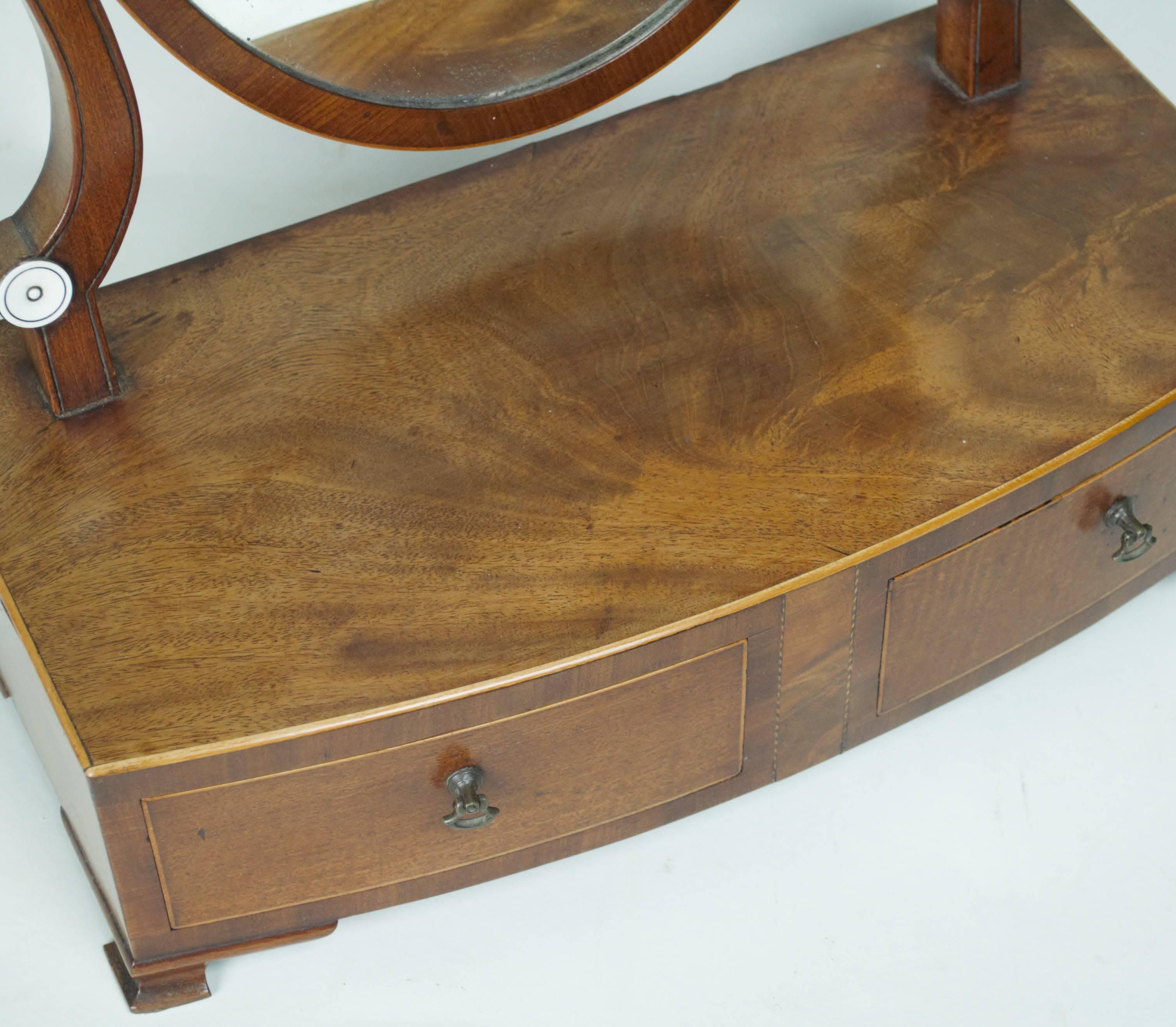 A good George III period mahogany, bow-fronted, box-base dressing table mirror with oval swing-plate above a bow-fronted base fitted with two small drawers and standing on ogee bracket feet. 
Crossbanded and with inlaid stringing.
