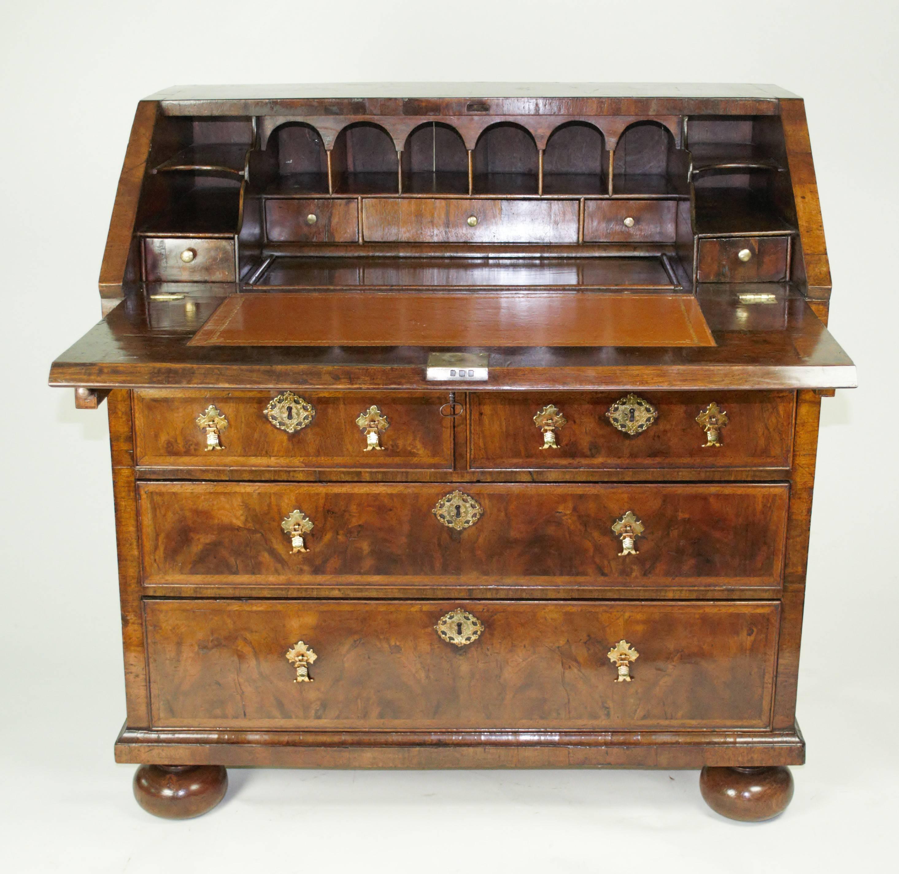 A good George I period walnut bureau. The fitted interior with a well, above two short and two long drawers, and standing on replaced bun feet. The whole cross-banded with herring-bone banding and of a good mellow color. Original brass