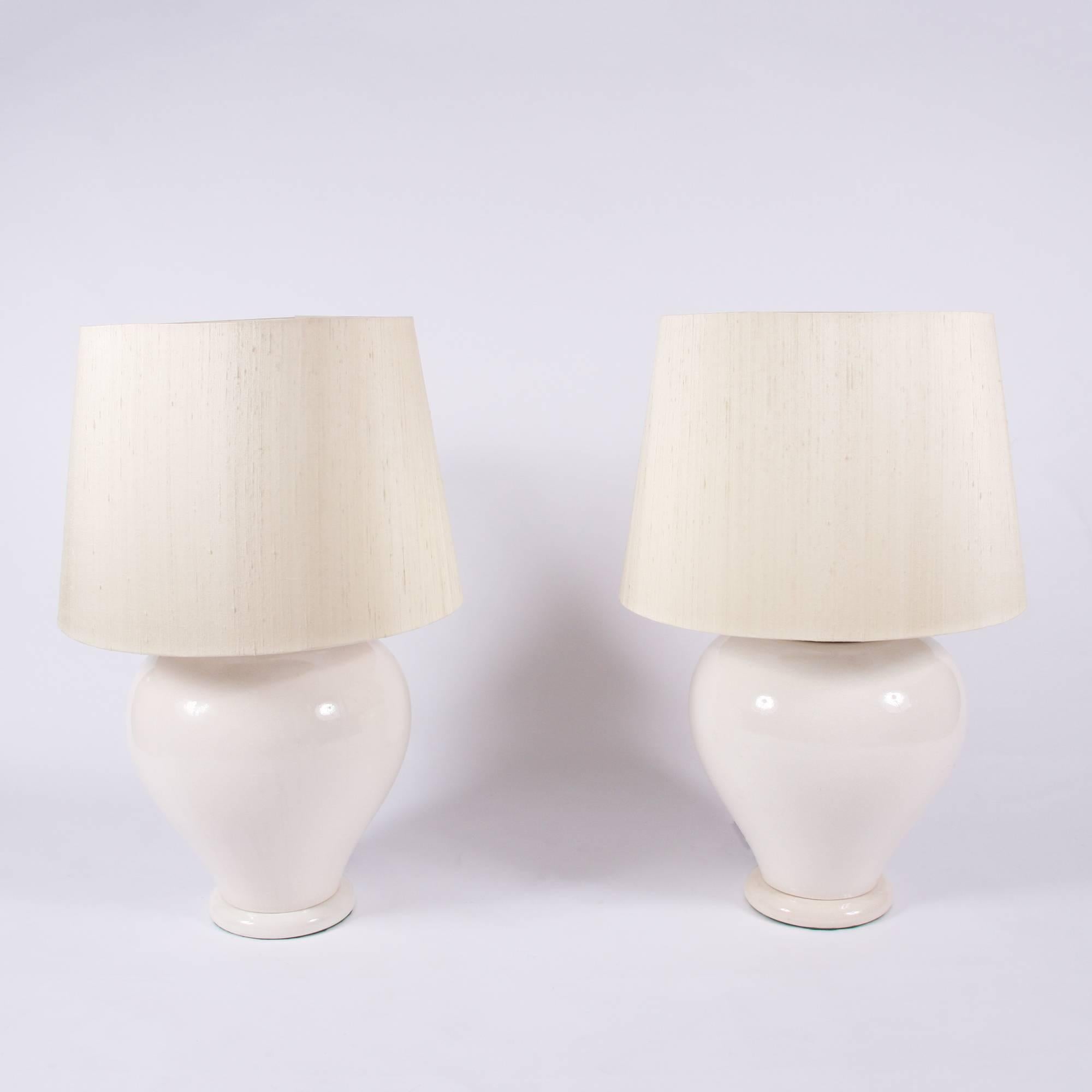 A fantastic pair of cream ceramic French table lamps. Large size ceramic bases with ivory silk hand made lamp shades. Re-wired.