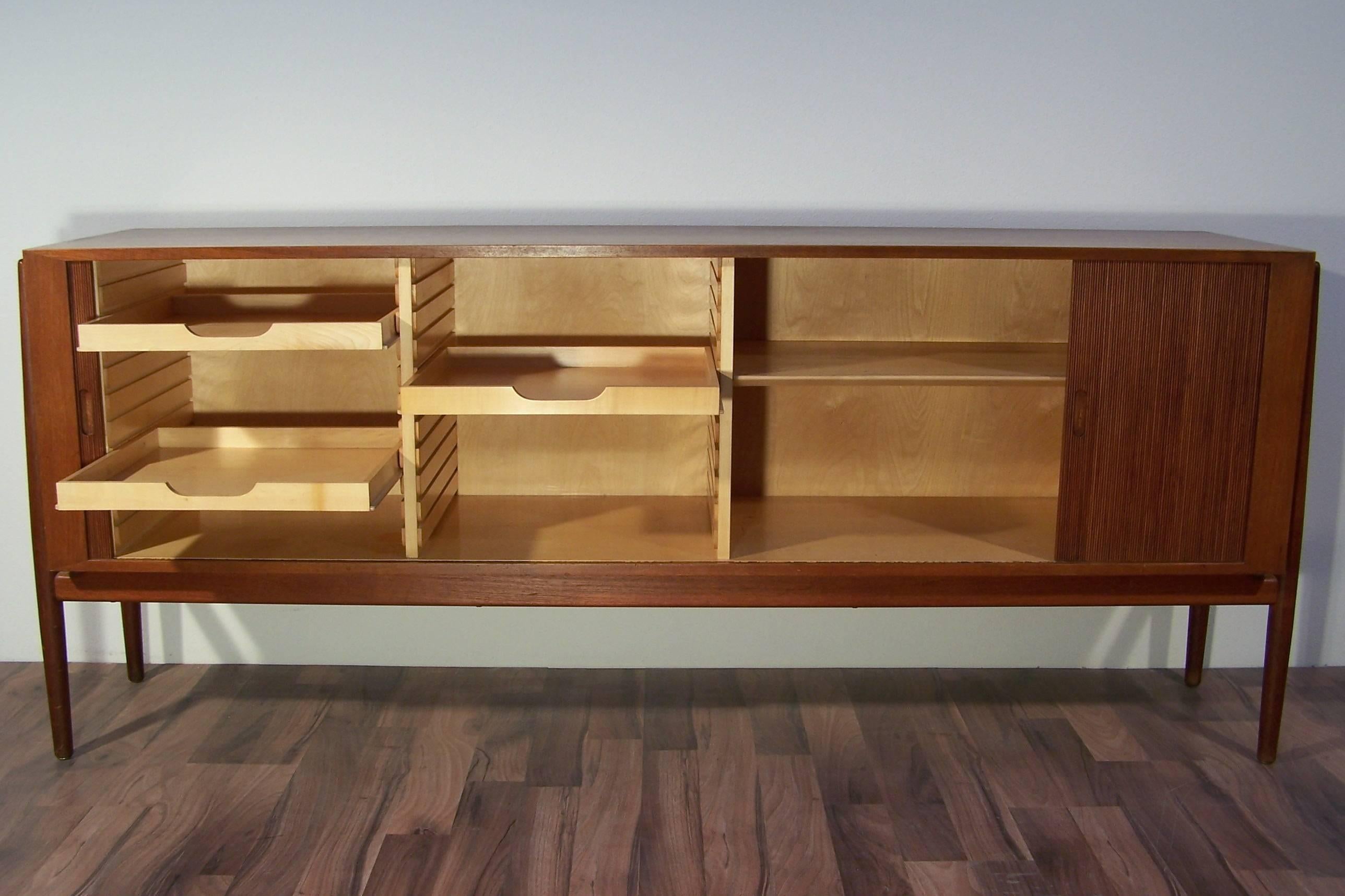 Finn Juhl designed this stunning sideboard circa 1954 for Niels Vodder. This sideboard has elegant tambour doors which open into the sides of the case.
The interior is made of birch wood and contains three drawers and one shelf. It has an