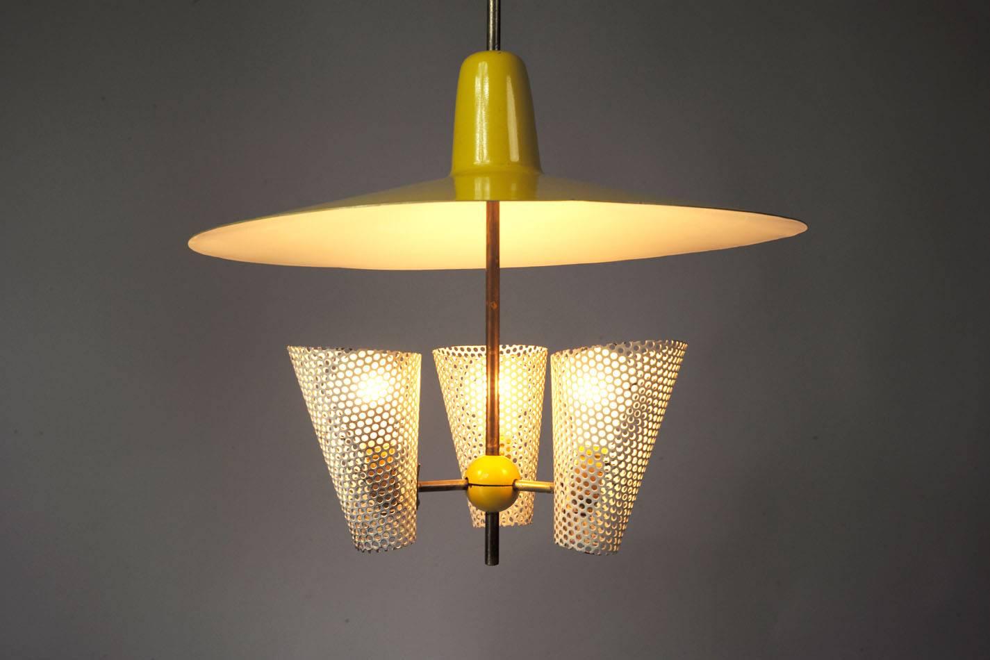 This vintage suspension lamp was made and manufactured during the 1950s by Stellar, assigned to Jacques Biny. It features three white painted perforated metal bulb shields covered by a bigger yellow and adjustable reflector. The lamp is in excellent