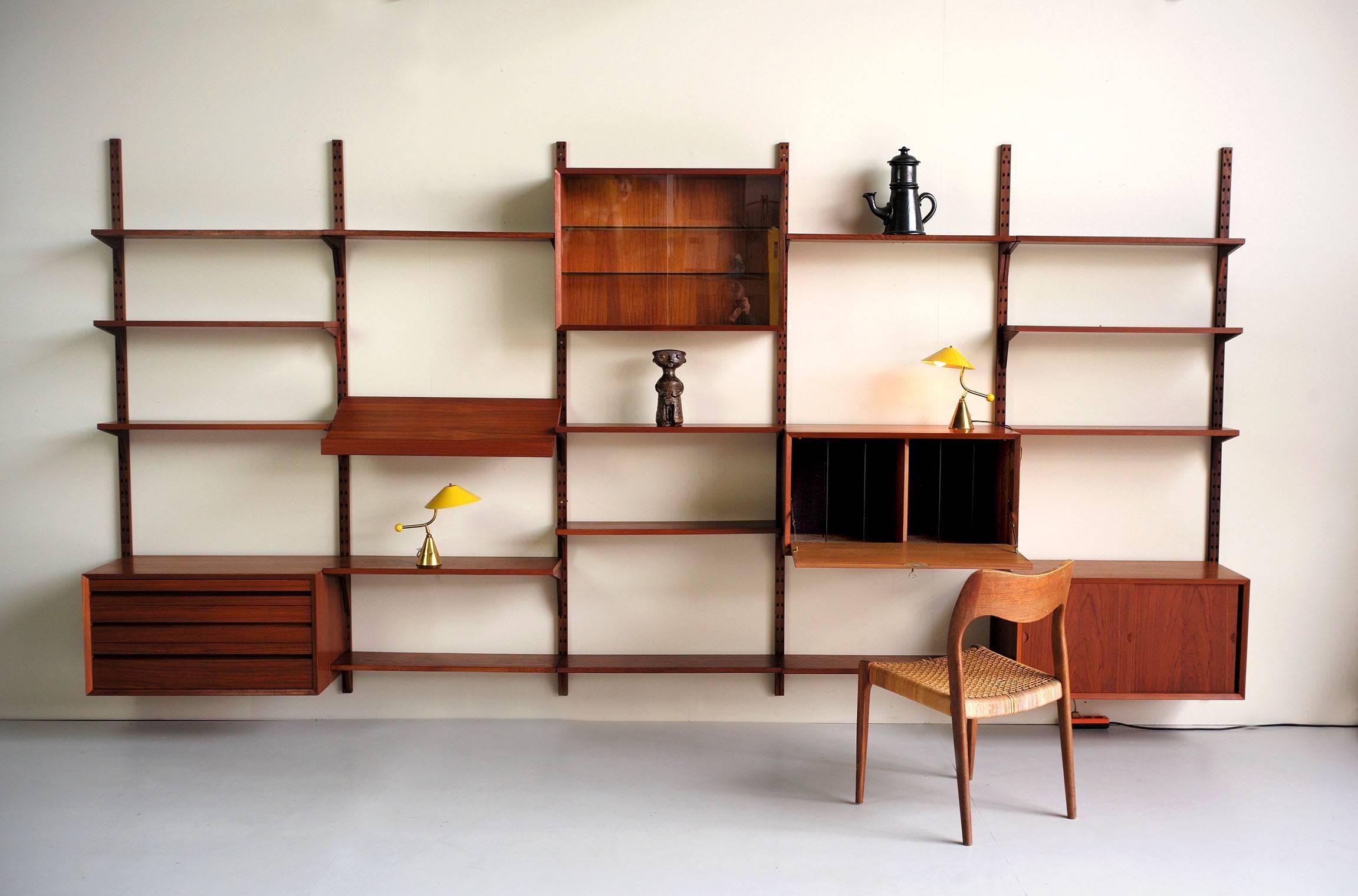 This Royal System modular teak wall unit was designed by Poul Cadovius and made in Denmark, circa 1960. It consists of seven uprights with a height of 202.5cm, four cabinets, including one with a desk flap, one with wooden sliding doors, one with