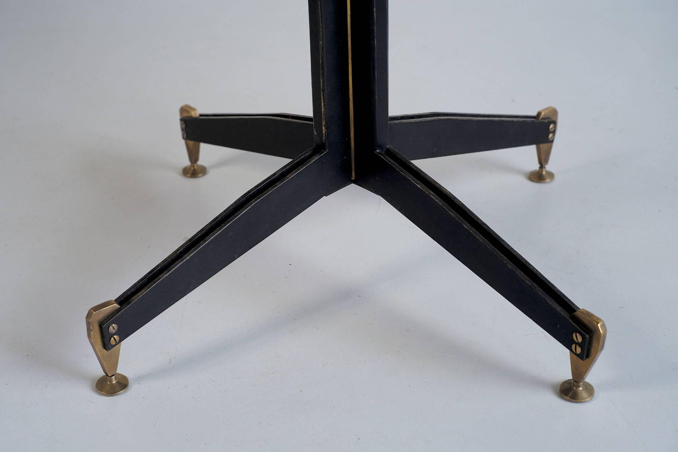 Round table in mahogany plywood with central base in blackened steel blades and gilded brass, Italy 1950. Solid brass clogs are held by two large visible screws, the central barrel is enhanced by a gilded brass tube. This table, attributed to