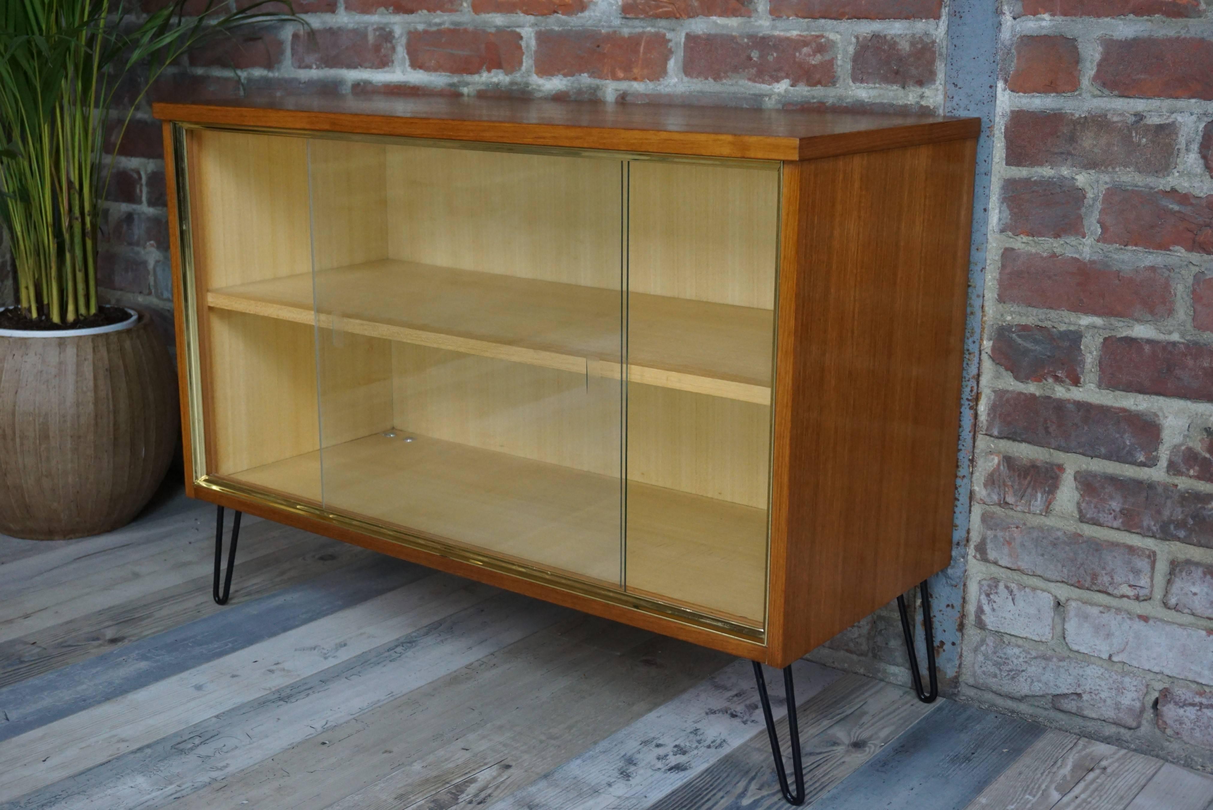 Nice teak storage cabinet from the 1950s, sliding glass doors, pin feet, underlined structure of a gilded metal frame. This piece of furniture brings together all the standards of a decor in the air. And of course, it is in excellent condition!