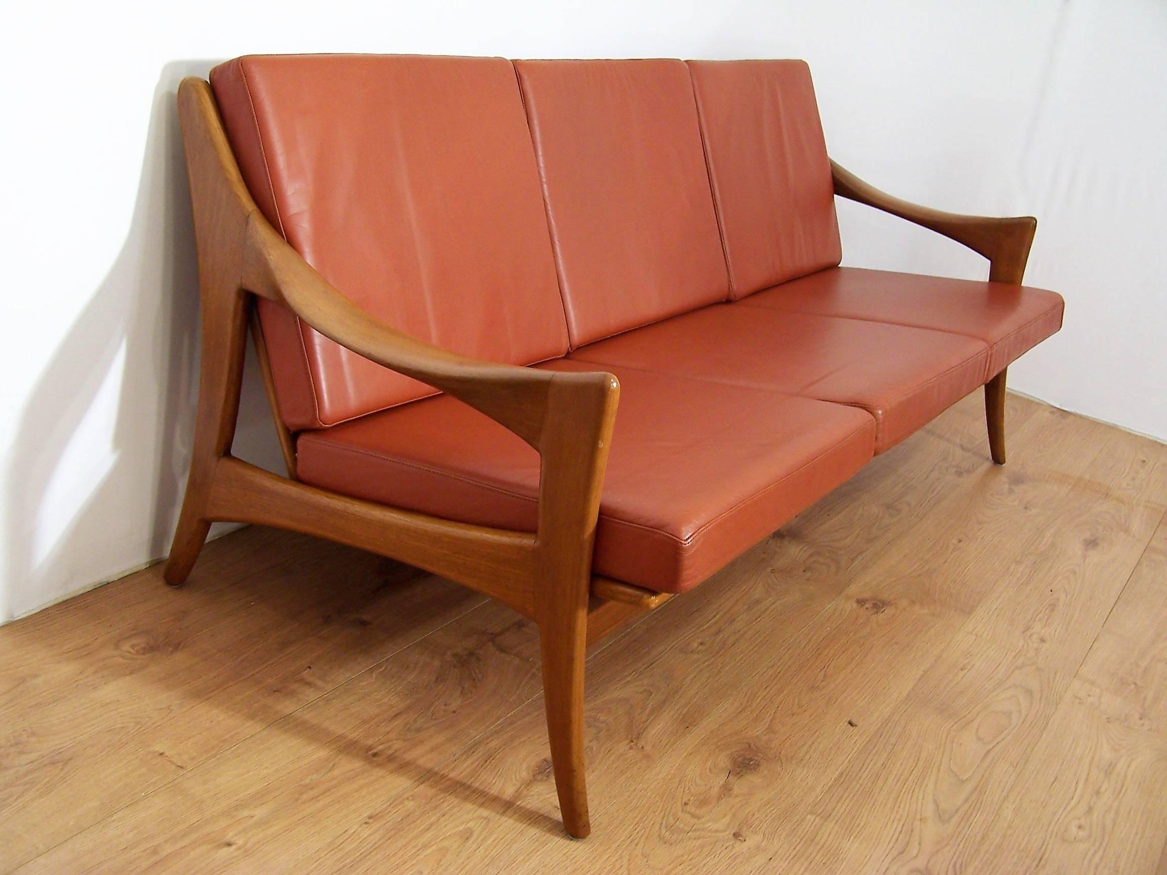 This three-seat sofa in Scandinavian style was produced in the 1950s or 1960s by the Dutch brand De Ster Gelderland. It is made from rounded teak, with cushions upholstered in red-tawny colored leather.