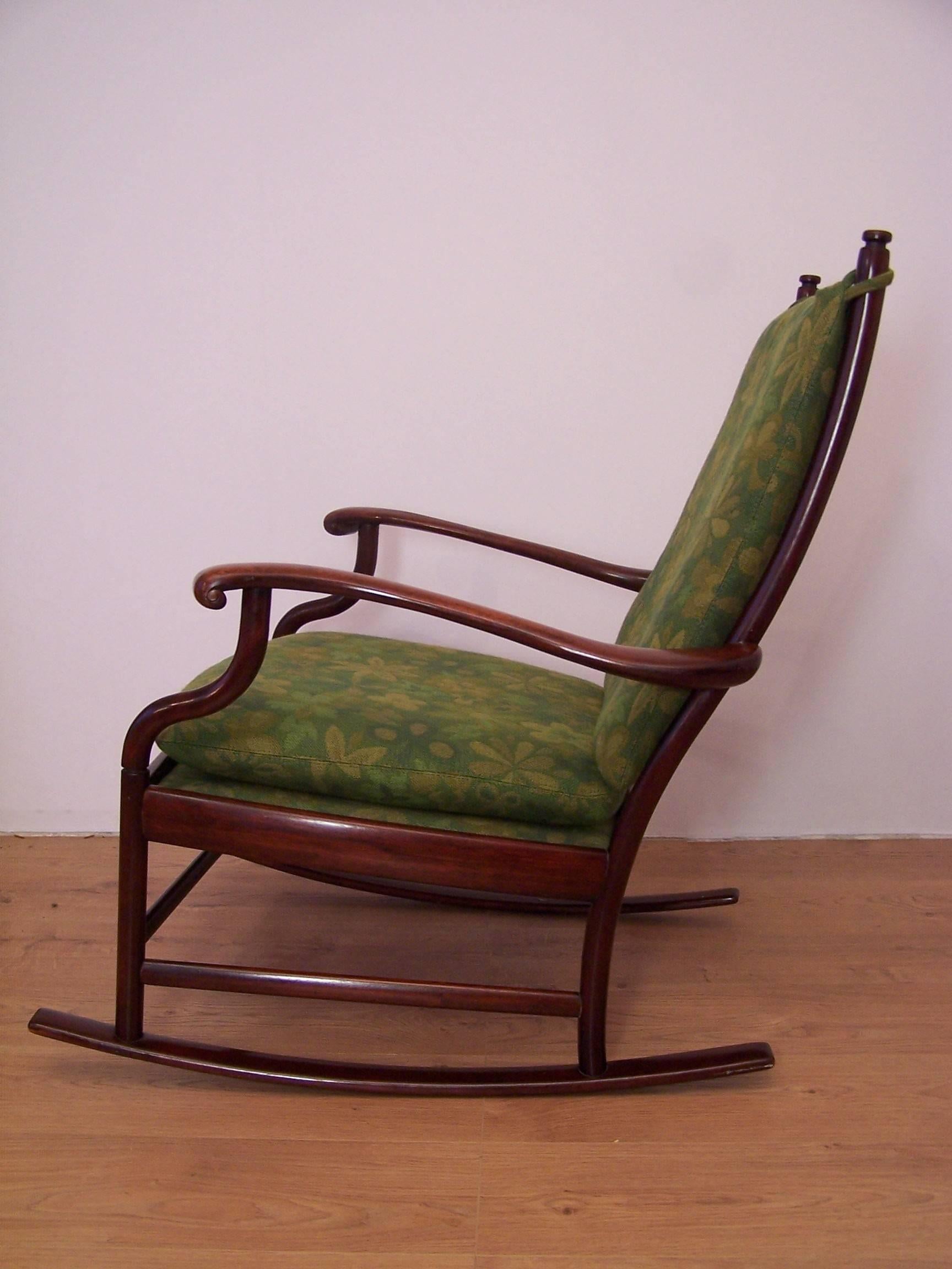 This rocking chair is made from solid rosewood and features two removable cushions which are covered with a green wool fabric that features a floral pattern.