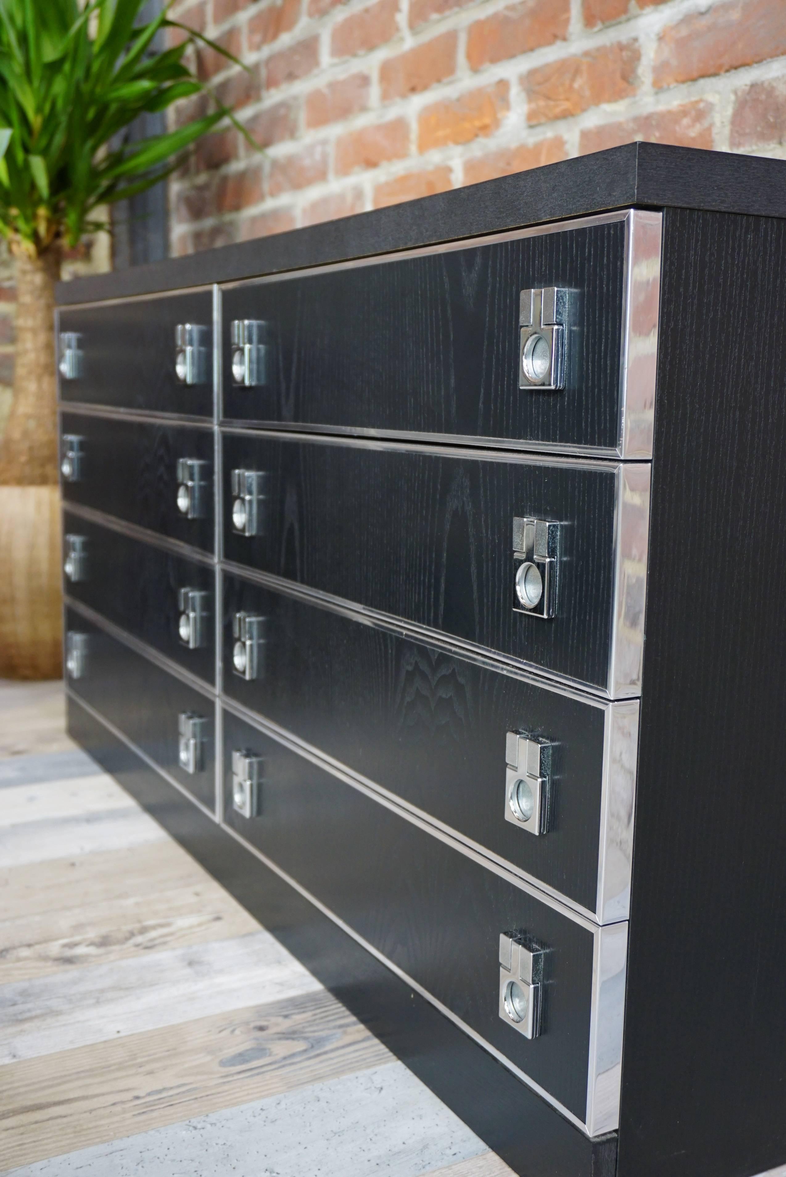 Simple lines and Minimalist design for this long black dresser with large storage space: eight drawers which have each subtly crafted facade, framed by a chrome edging and chrome metal handle, too. In very good state of conservation.
