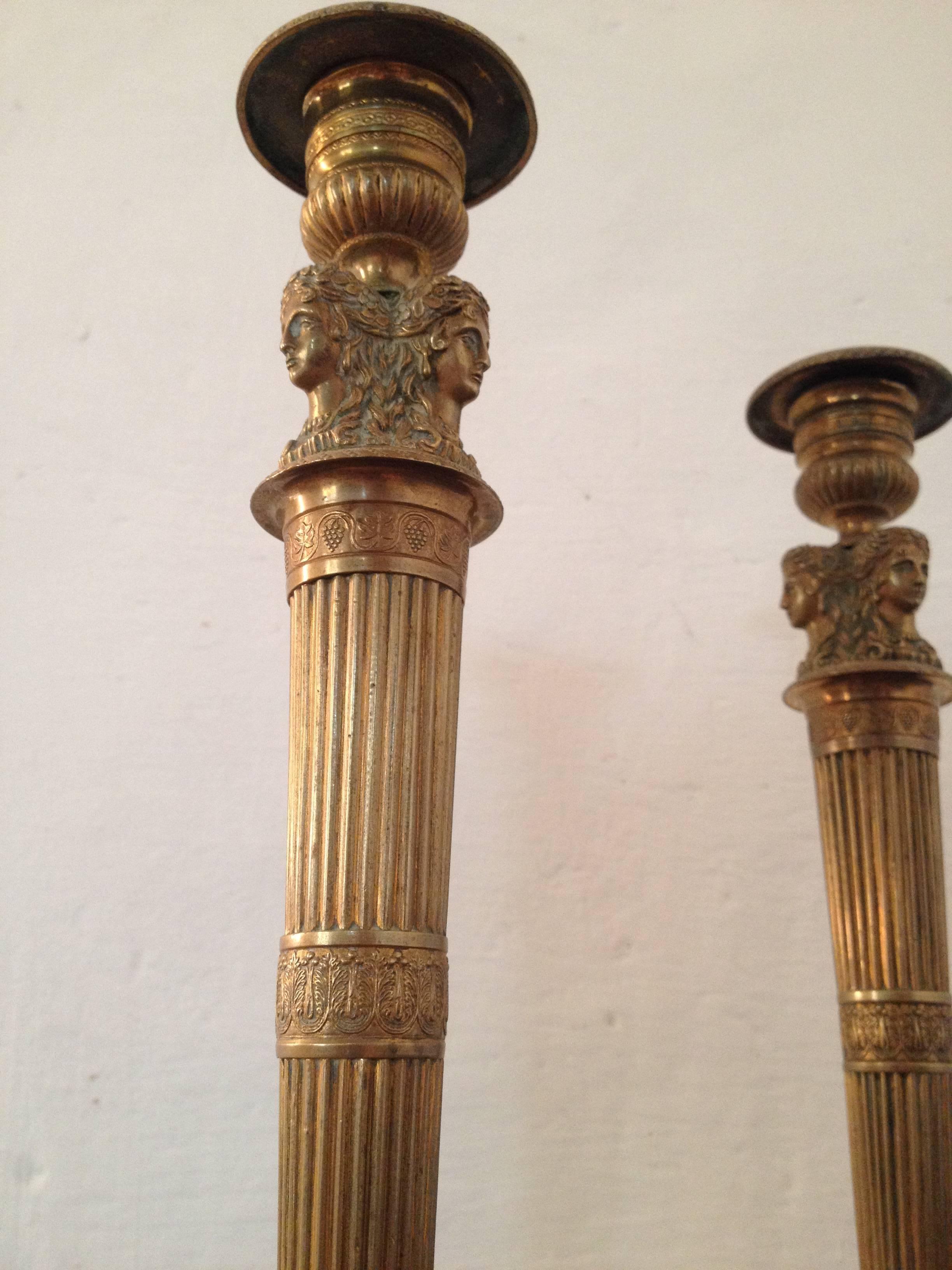 Pair of candlesticks in gilt and sculpted bronze, adorned with three cariatids set above a tapered shaft.
The sockets of the candlesticks are intricately sculpted with beading and stylized foliage. Each candlestick is set on a circular base with a