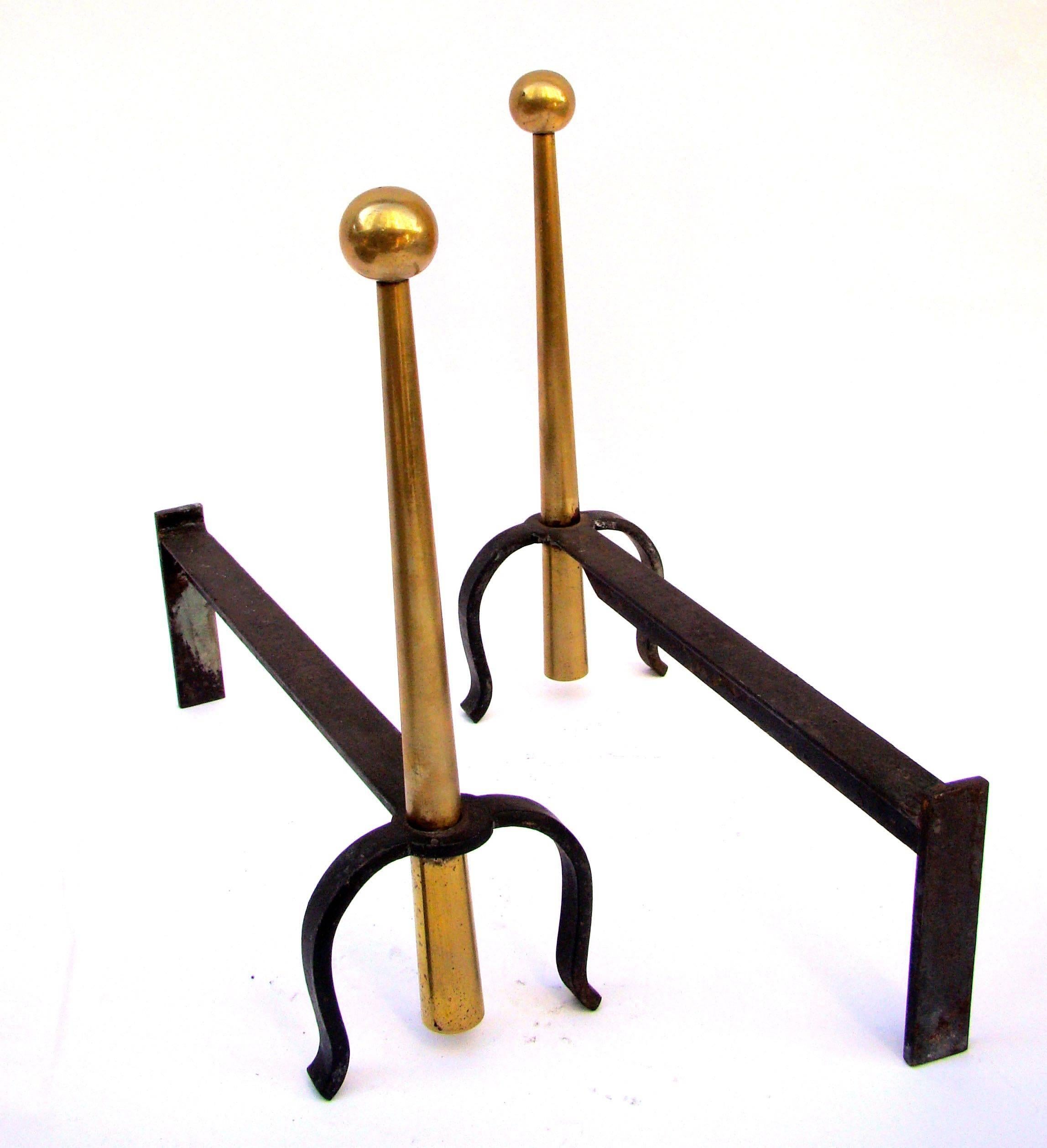 Pair of andirons in the style of Jean Royère in wrought iron and brass surmounted by large spheres, circa 1950s-1960s.