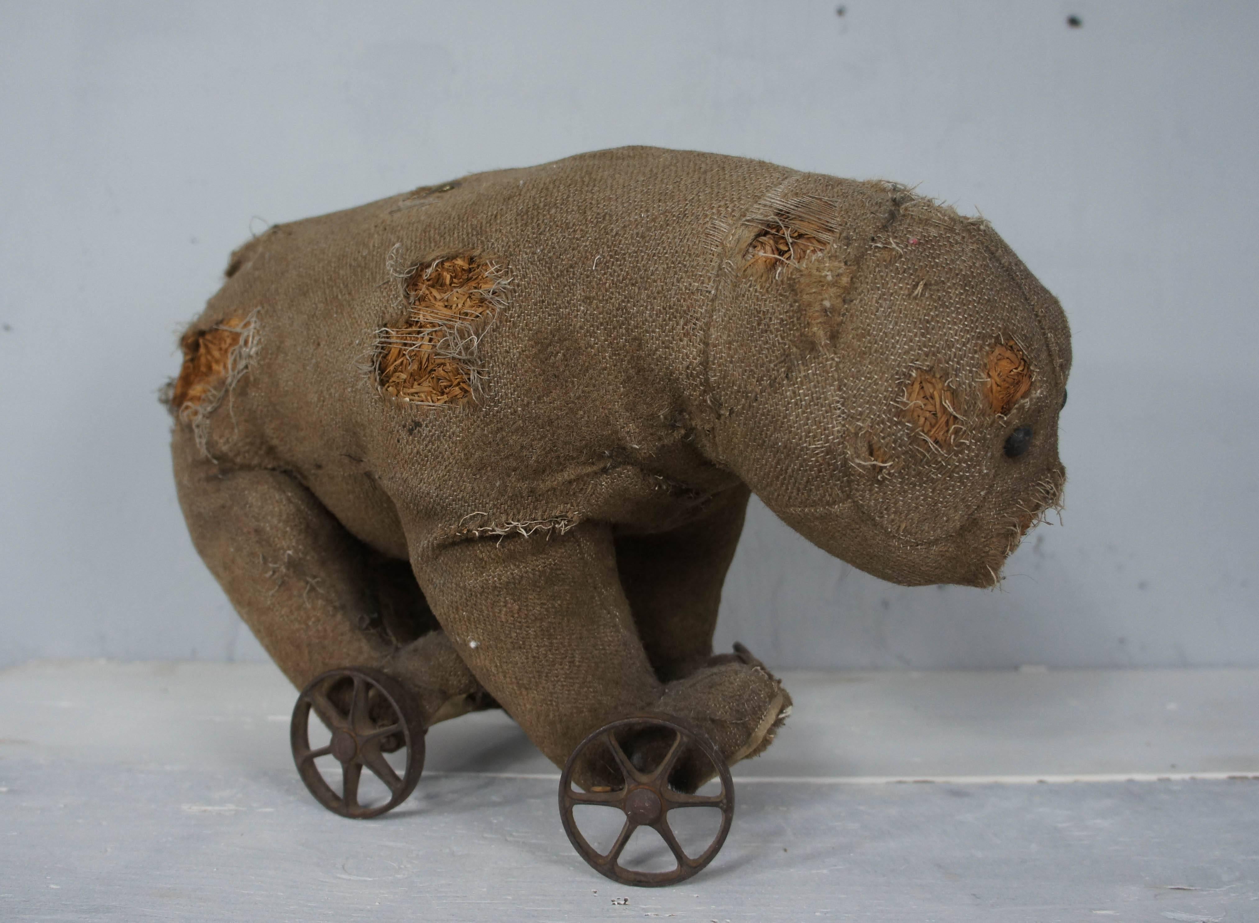Absolutely adorable very early Steiff bear on cast iron wheels. He must have been very much loved and played with during his existence, as shown by the amount of wear he has. He has lost his mohair fur but retains hessian cloth with some holes over