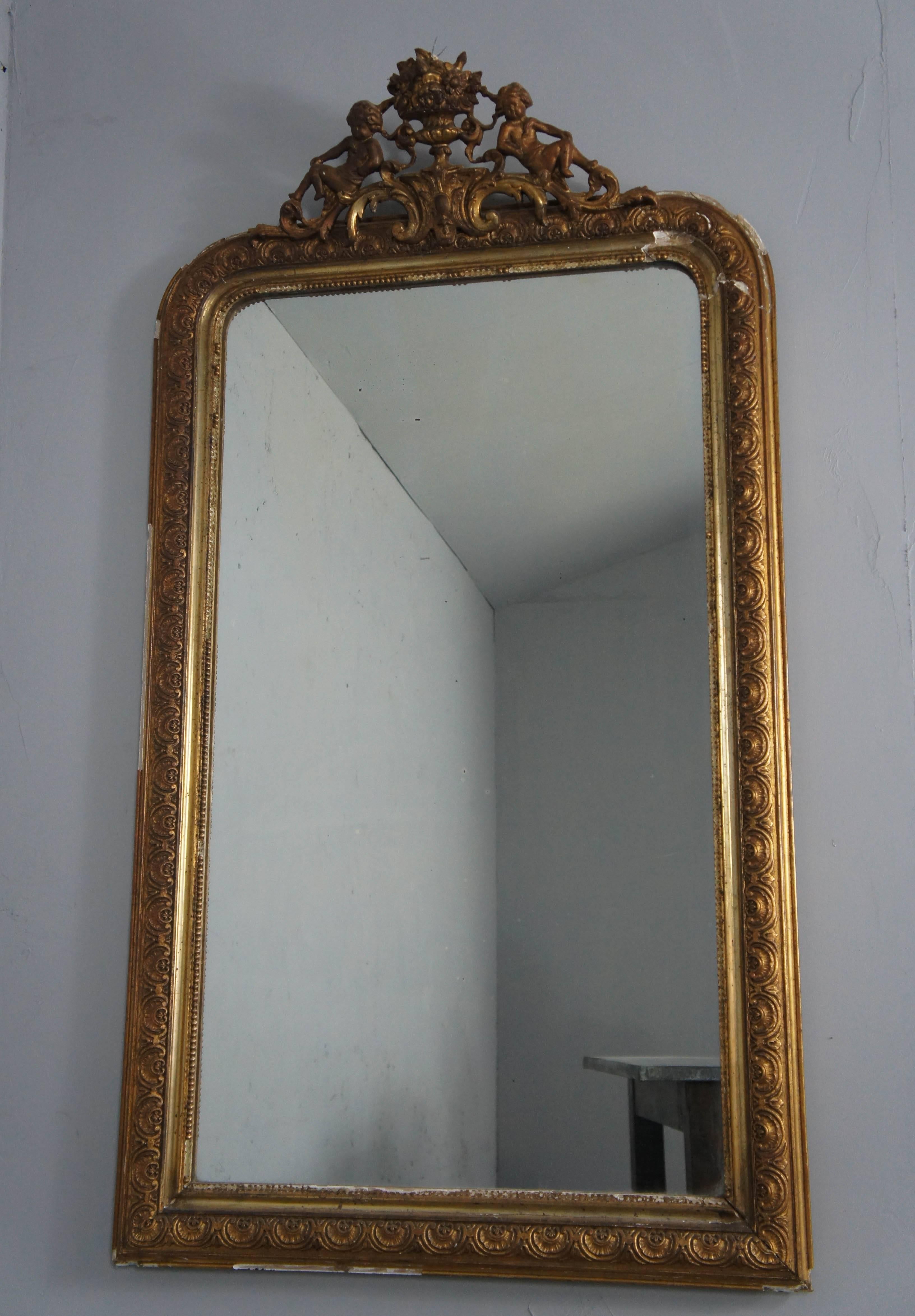 Beautiful 19th century Louis Philippe wood and gesso overmantel mirror. The gilt frame is crested with a highly decorative pair of cherubs with an arrangement of flowers or urn.
It retains original the mirror glass, which is slightly foxed and