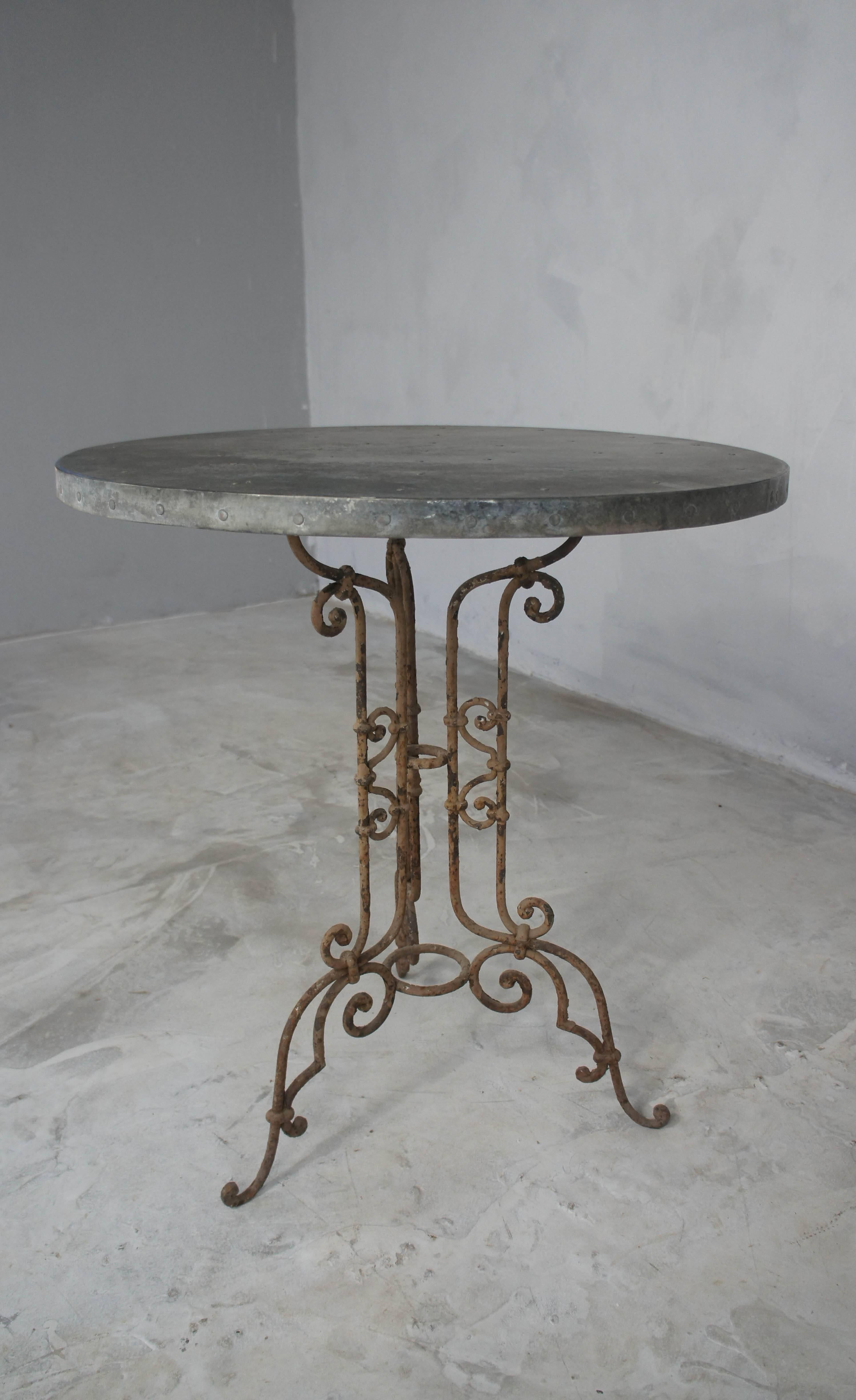Very pretty wrought iron garden table with aged zinc top. Base has flaky brown paint and very decorative ironwork.
Perfect small table for the garden or patio.