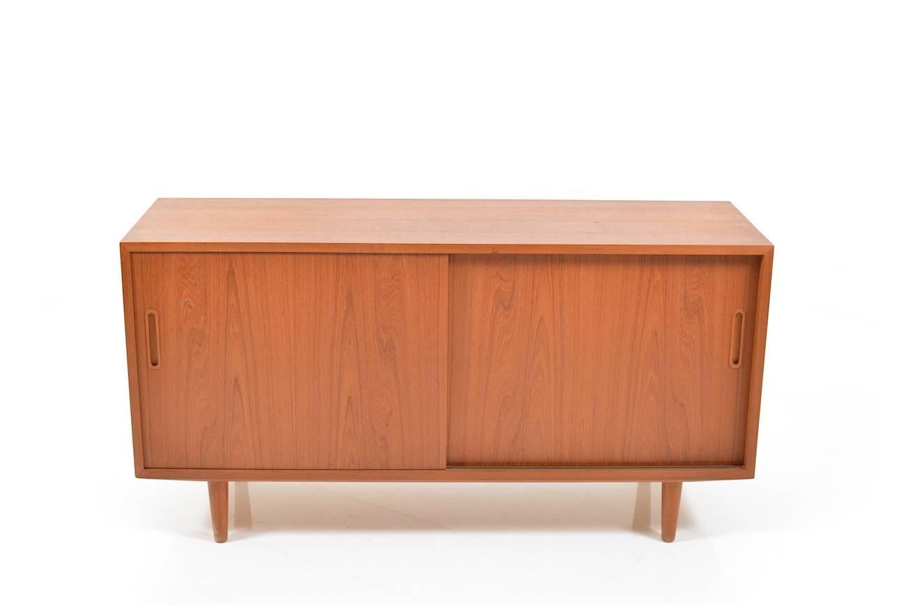 Small teak wooden sideboard. Designed Poul Hundevad. Front with two sliding doors. Behind the doors with shelves. Fine Danish vintage quality.