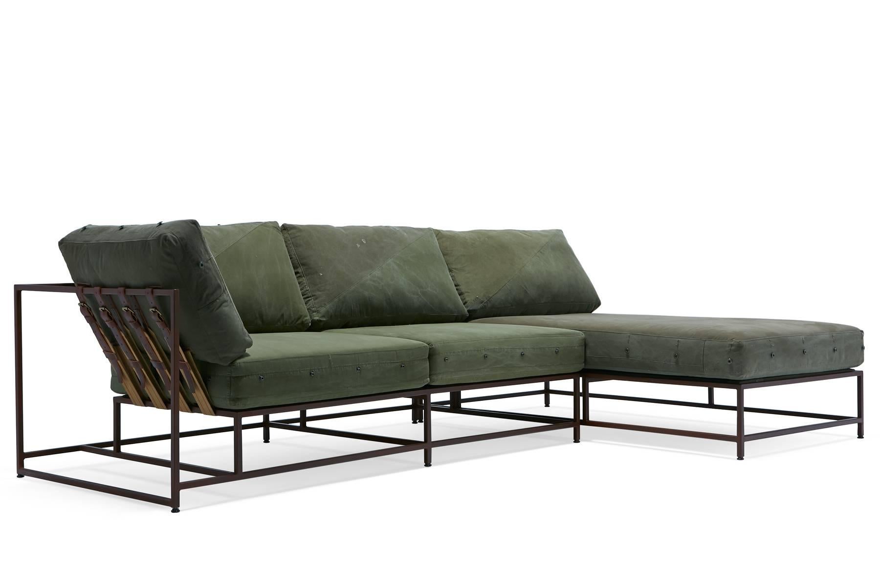 A sectional version of the Inheritance collection sofa made with military canvas upholstery and a marbled rust frame finish. The belts are made with cotton webbing, oxblood brown leather and antique brass buckles. This design is made in two pieces