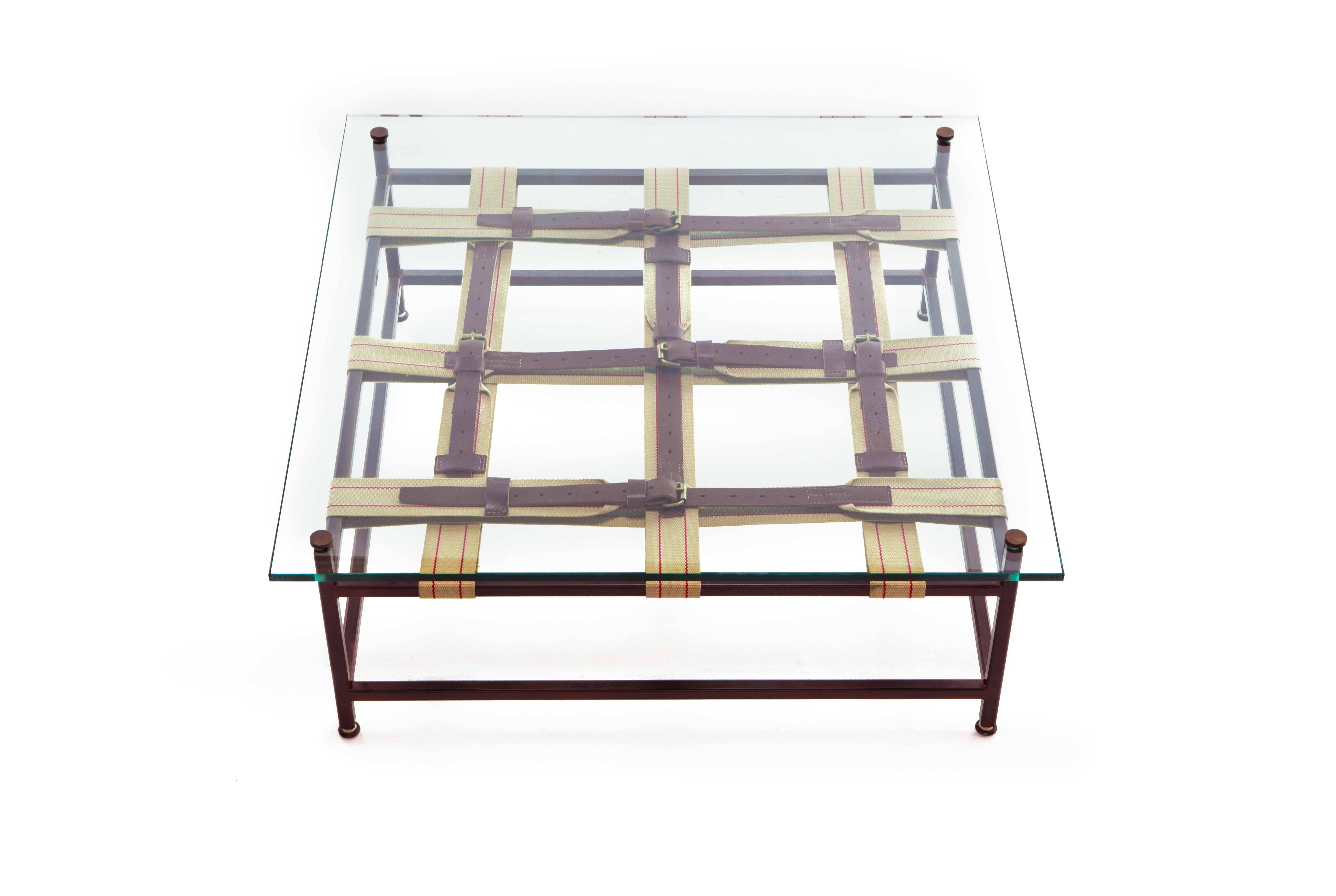 A glass topped coffee table that utilizes the signature Inheritance collection belts. This version was made to pair with the military canvas and rust sofa. The steel frame has a marbled rust finish and tan and red webbing belts with oxblood leather