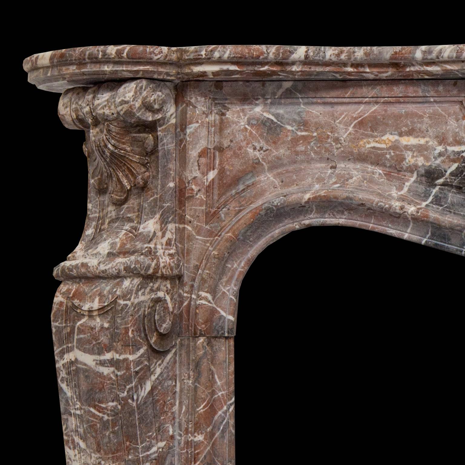 19th century Louis XV style beautiful fireplace sculpted in a soft colored Rouge Royal marble. The finely carved shelf rests on a serpentine front, with a rocaille shell framed by flowers. The jambs are hand-carved in the form of curved and tapered
