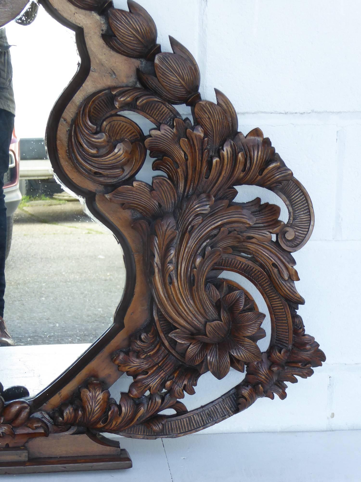 Zum Verkauf steht ein hochwertiger, stark geschnitzter Spiegel aus dem 19. Jahrhundert. Mit einem geschnitzten Maskenmotiv auf der Oberseite, hat der Spiegel unglaublich kunstvolle florale Schnitzereien auf beiden Seiten, die einen geformten Spiegel