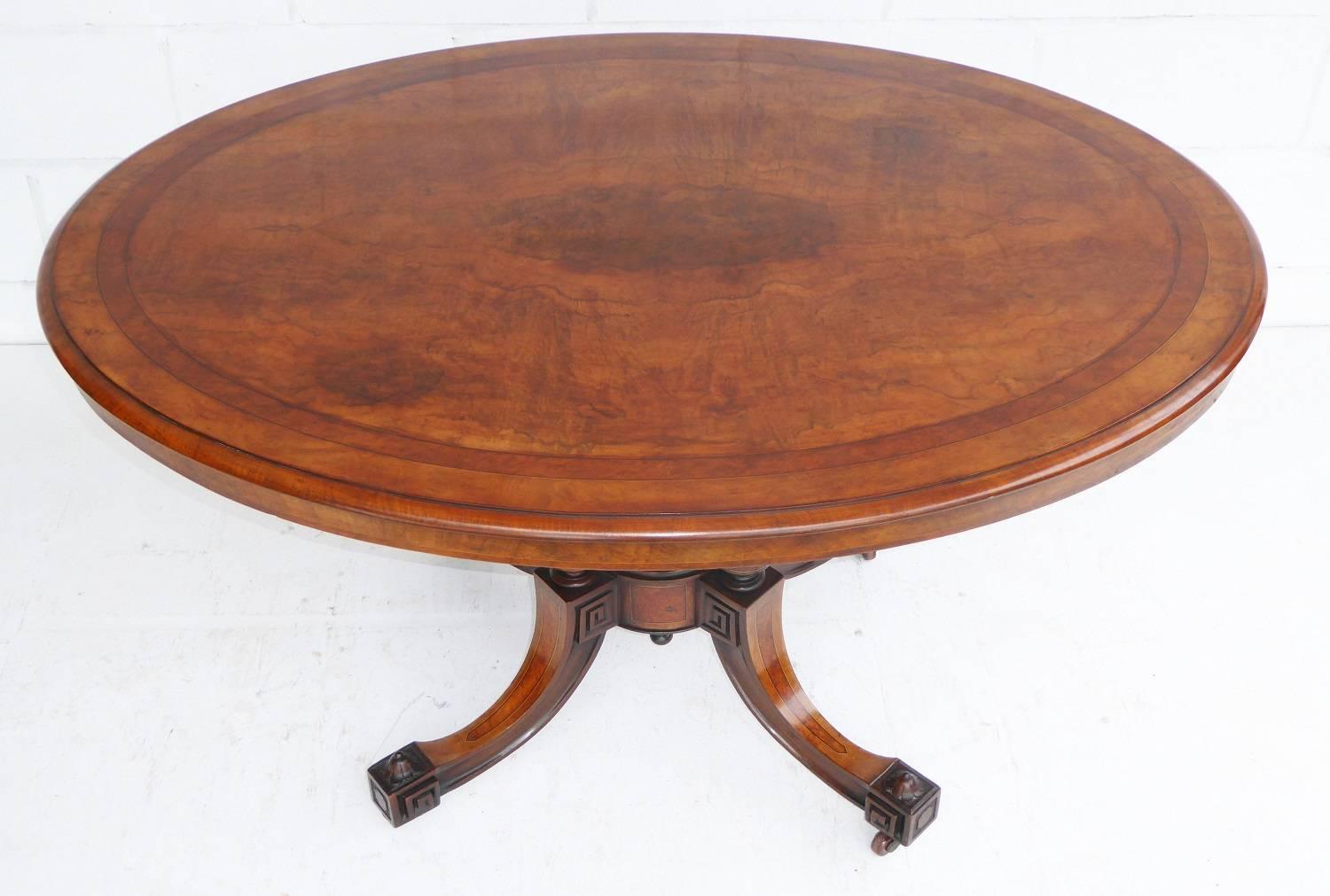 For sale is a good quality Victorian burr walnut and inlaid oval loo table. The top of the table is inlaid and banded above a birdcage base. The base has four columns with an ornate finial to the centre, standing on four satinwood banded splayed