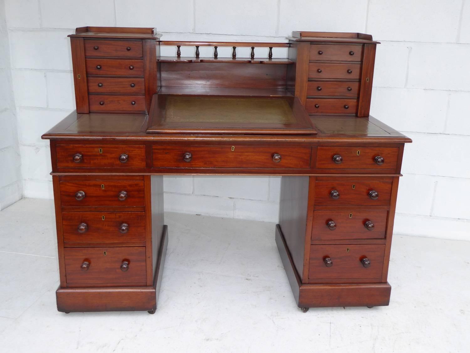 For sale is a Victorian mahogany Dickens desk. The top of the desk has two sets of four small drawers, with a side locker, as well as three leather writing surfaces, each decorated with gold tooling. The centre of which rises to reveal storage