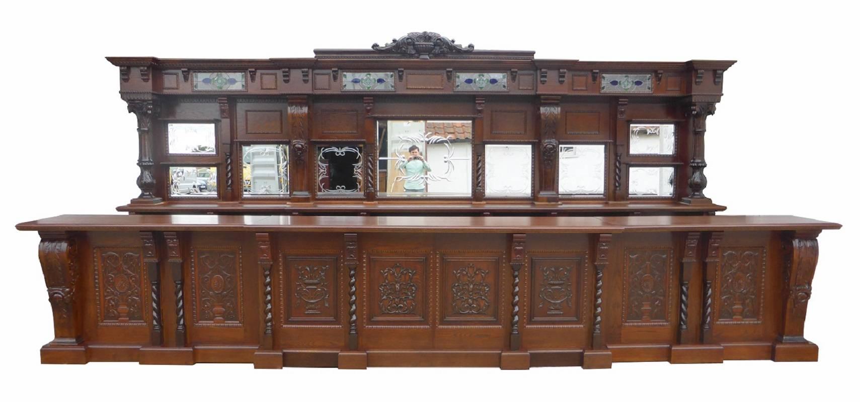 For sale is a superb quality 5 meter (18ft) commercial oak antique style bar. The top of the bar has an intricately carved pediment in the form of a carved urn with flowers. Below this the bar is fitted with four leaded glass panels, separated by